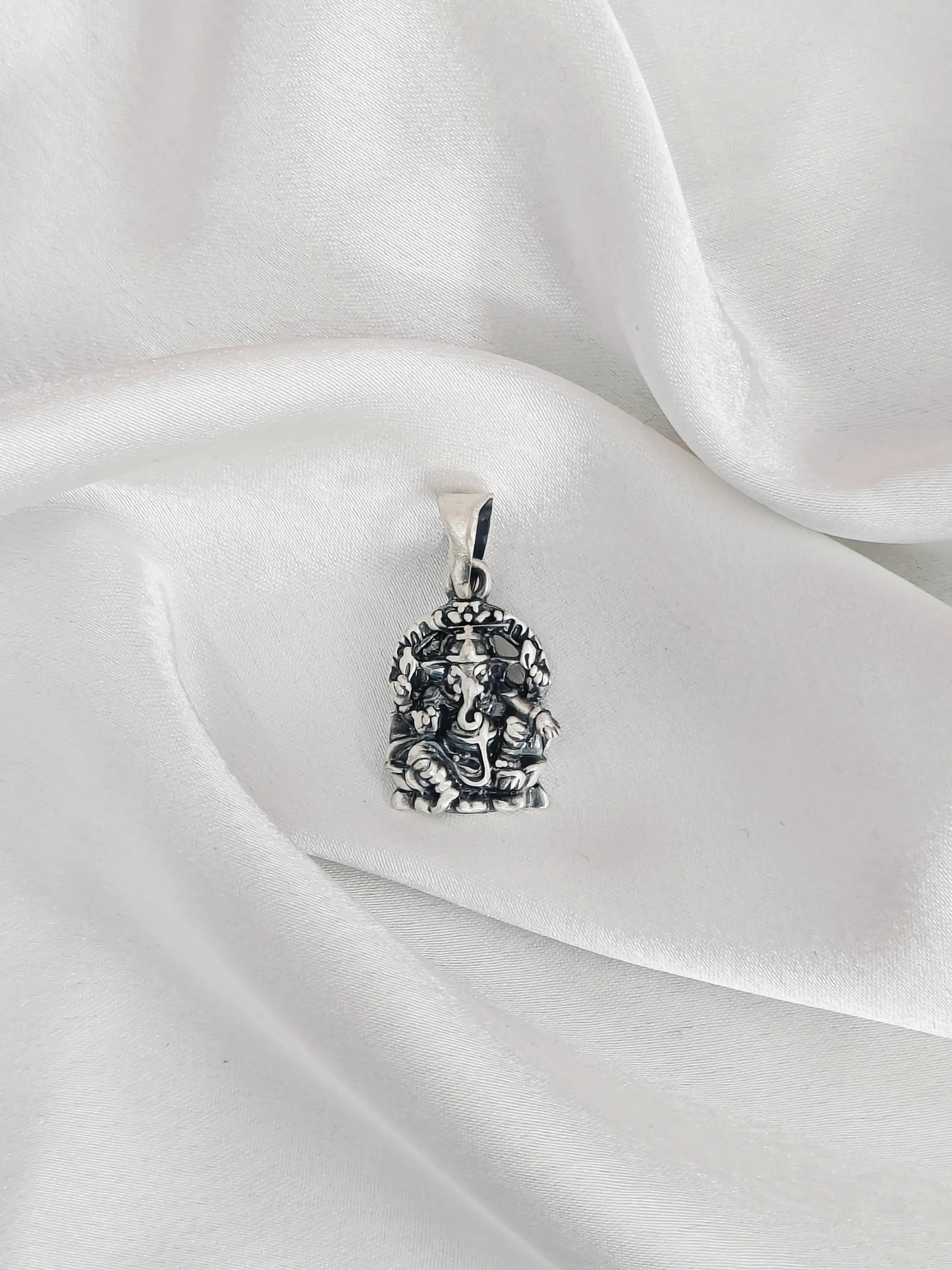 Silver pendant with intricate design on a white satin background