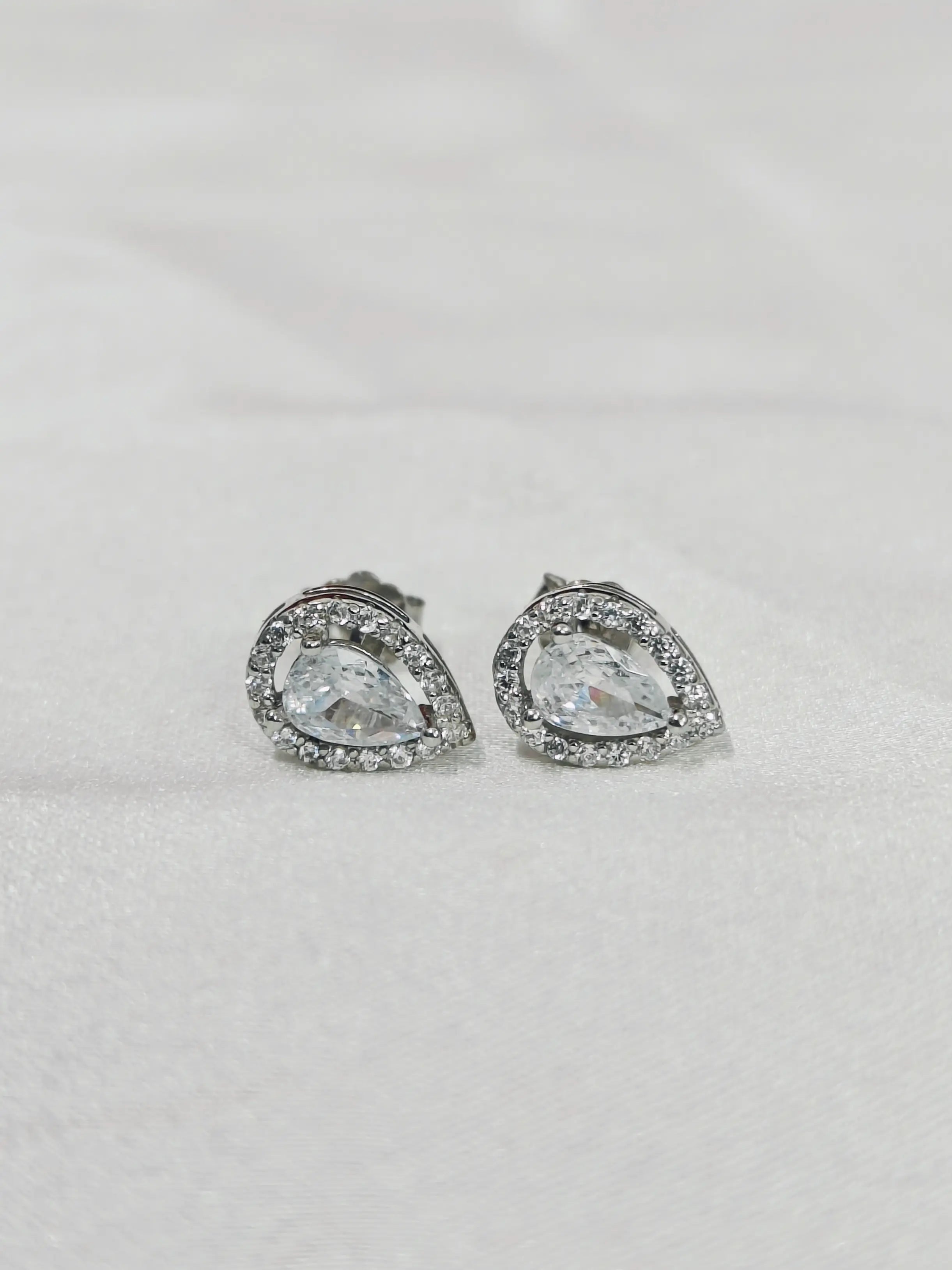Pair of teardrop-shaped earrings with clear gemstones on a light gray background