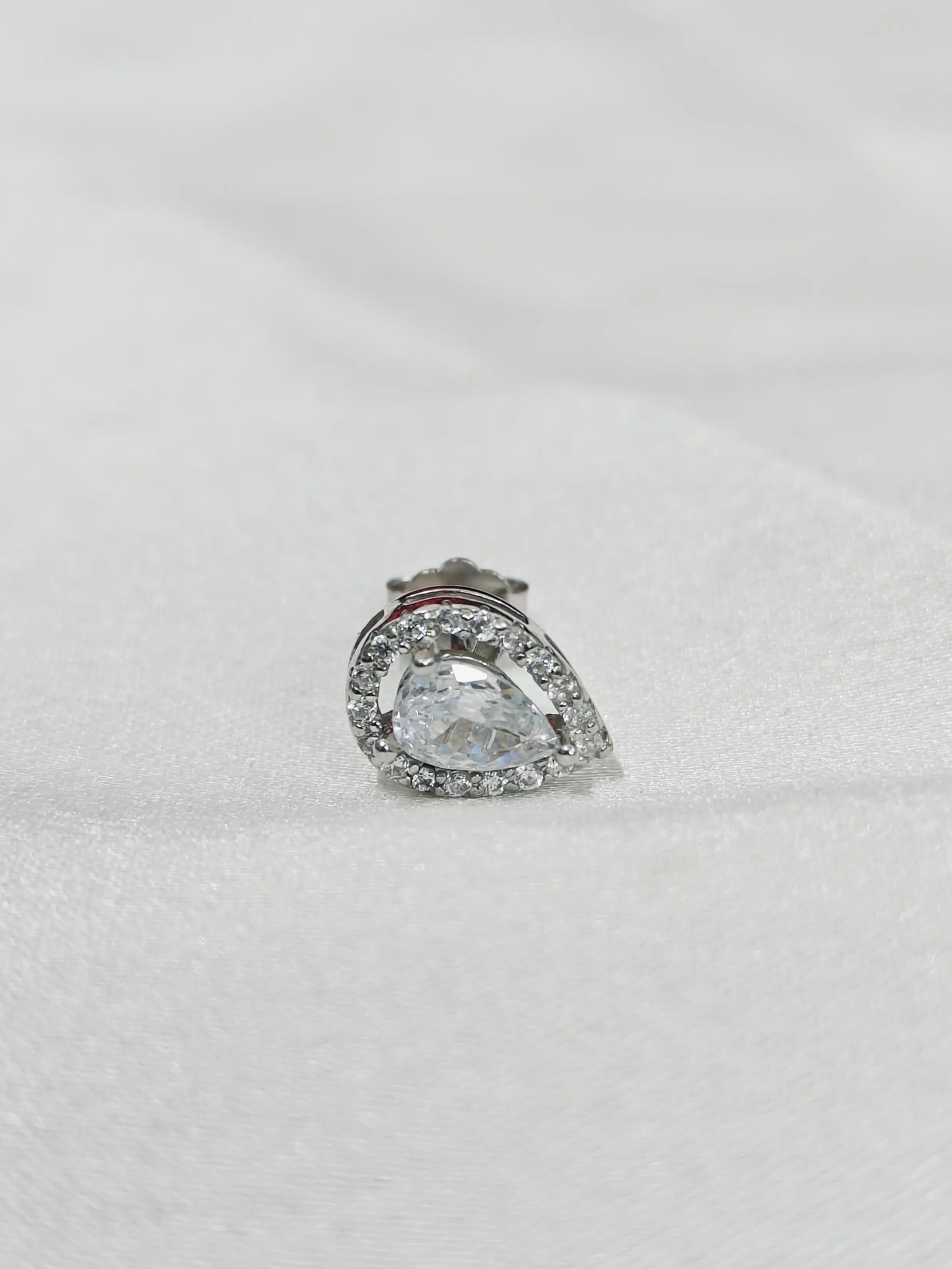 Silver teardrop-shaped earring with clear gemstone on a light gray background