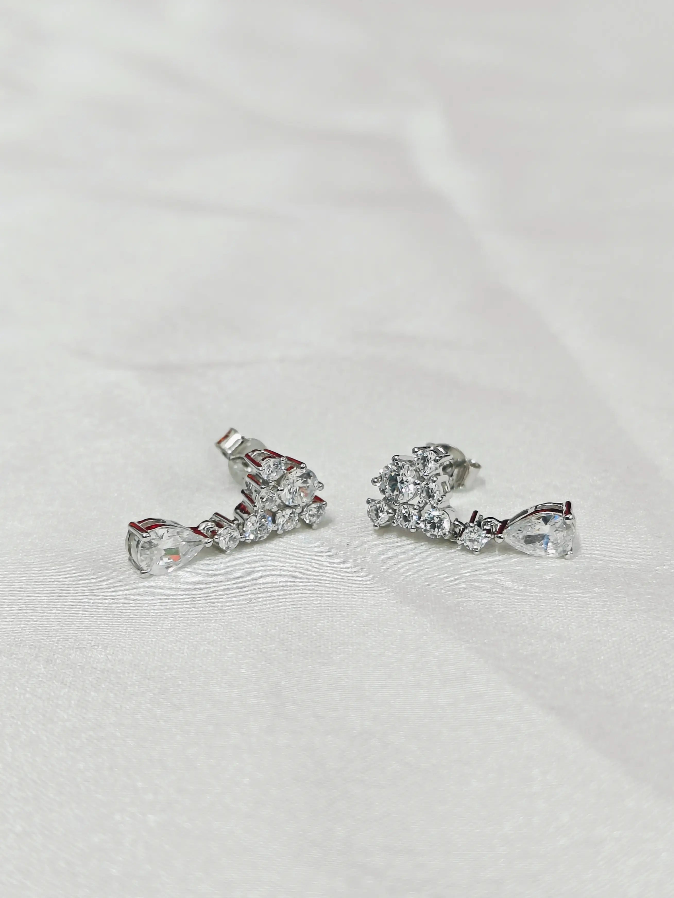 Pair of silver earrings with clear gemstones on a light gray background