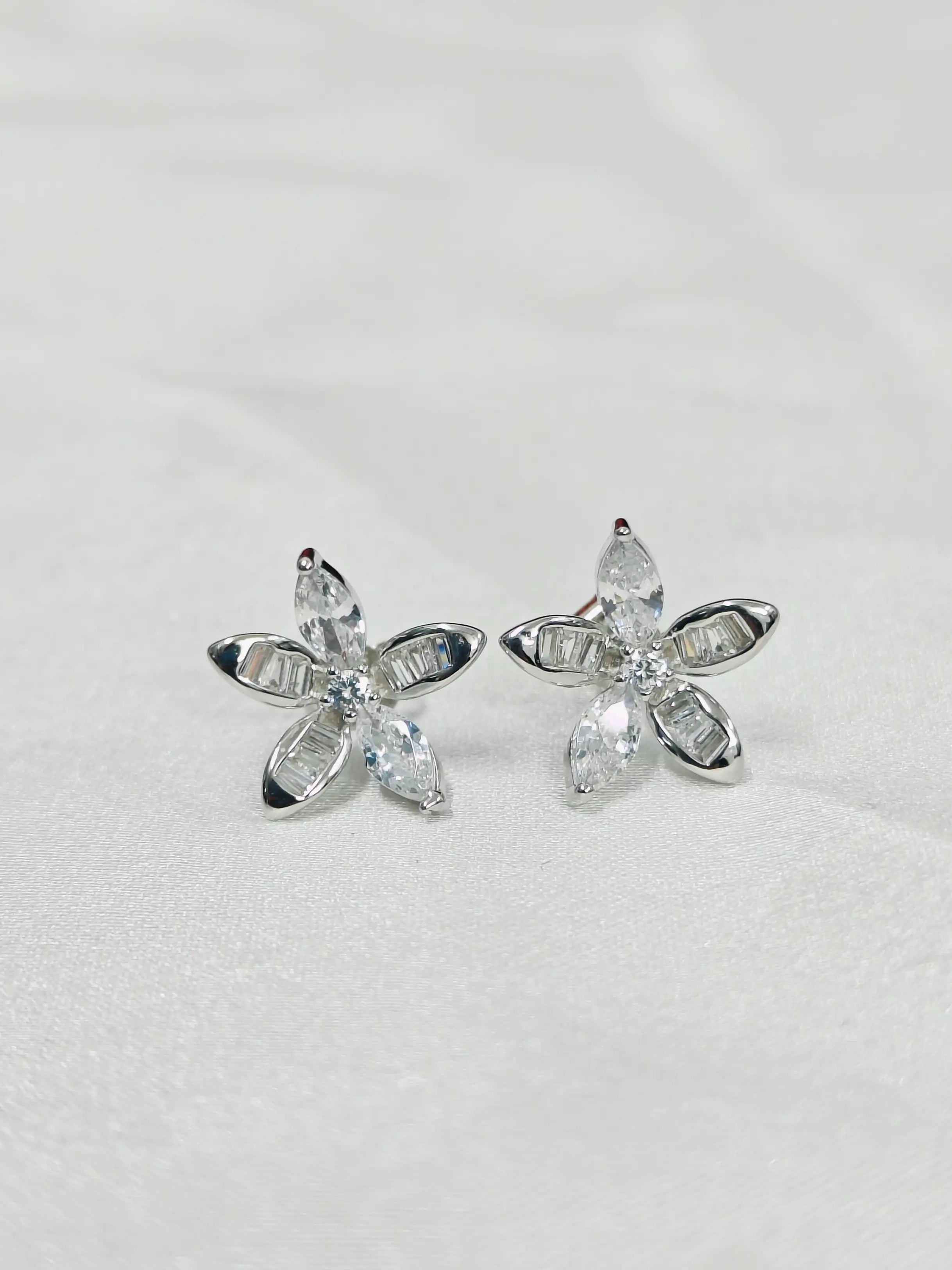 Silver flower-shaped earrings with clear gemstones on a light gray background
