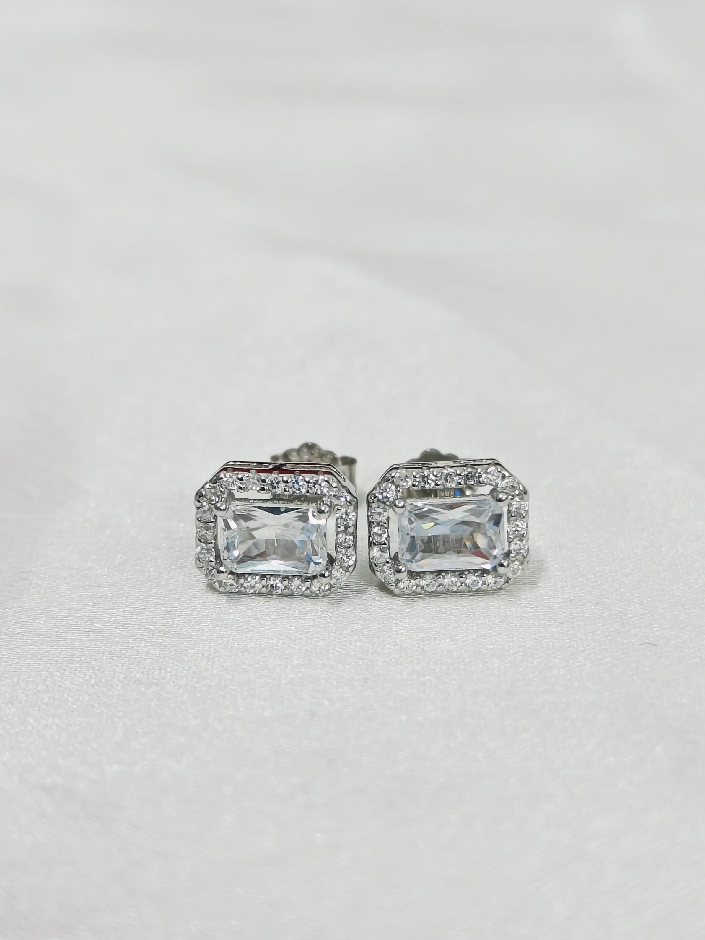 Pair of silver earrings with rectangular gemstones on a light gray background