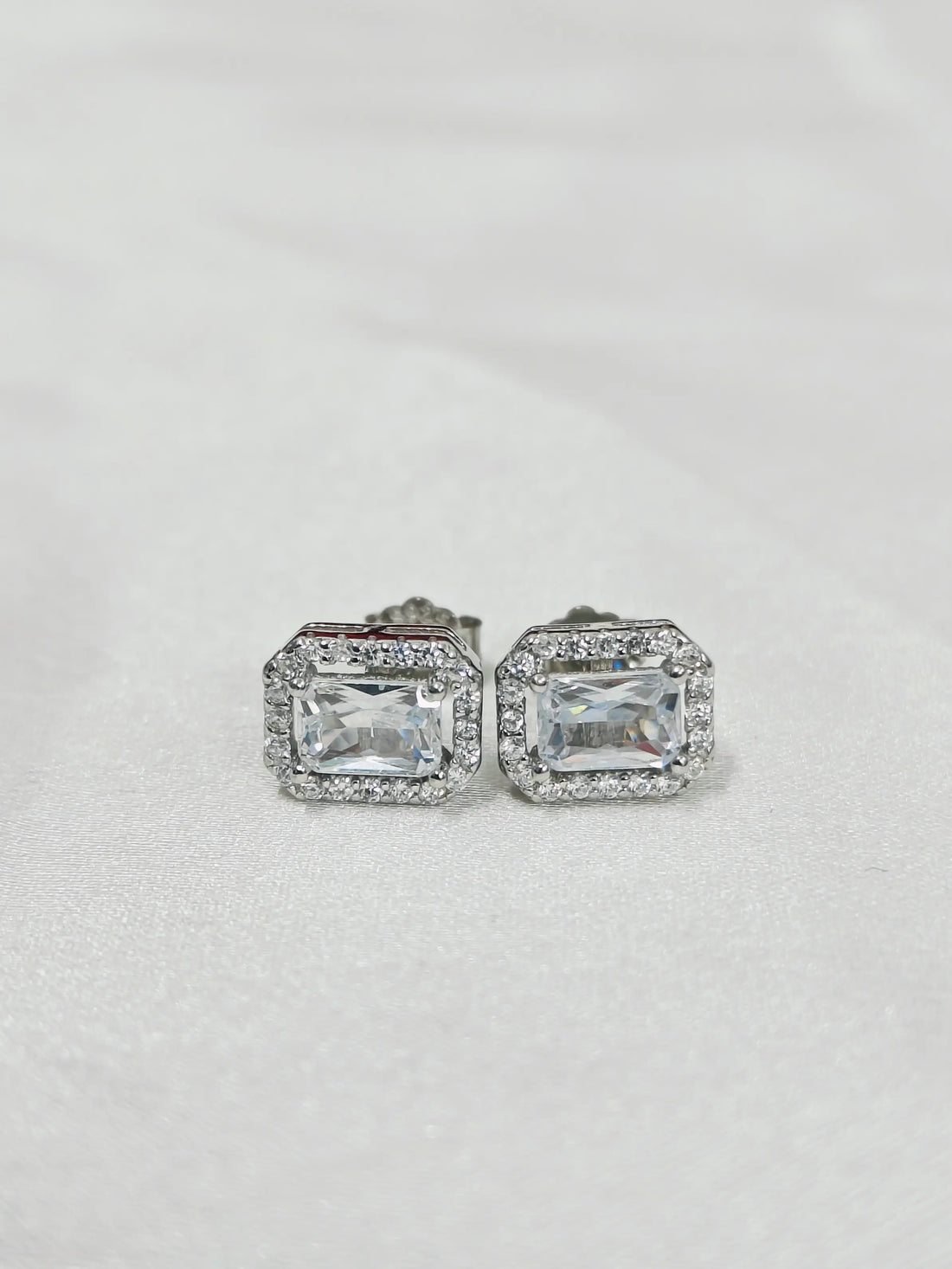 Pair of silver earrings with rectangular gemstones on a light gray background