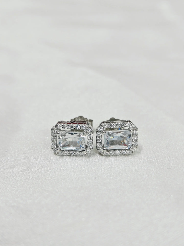 Pair of silver earrings with rectangular gemstones on a light gray background