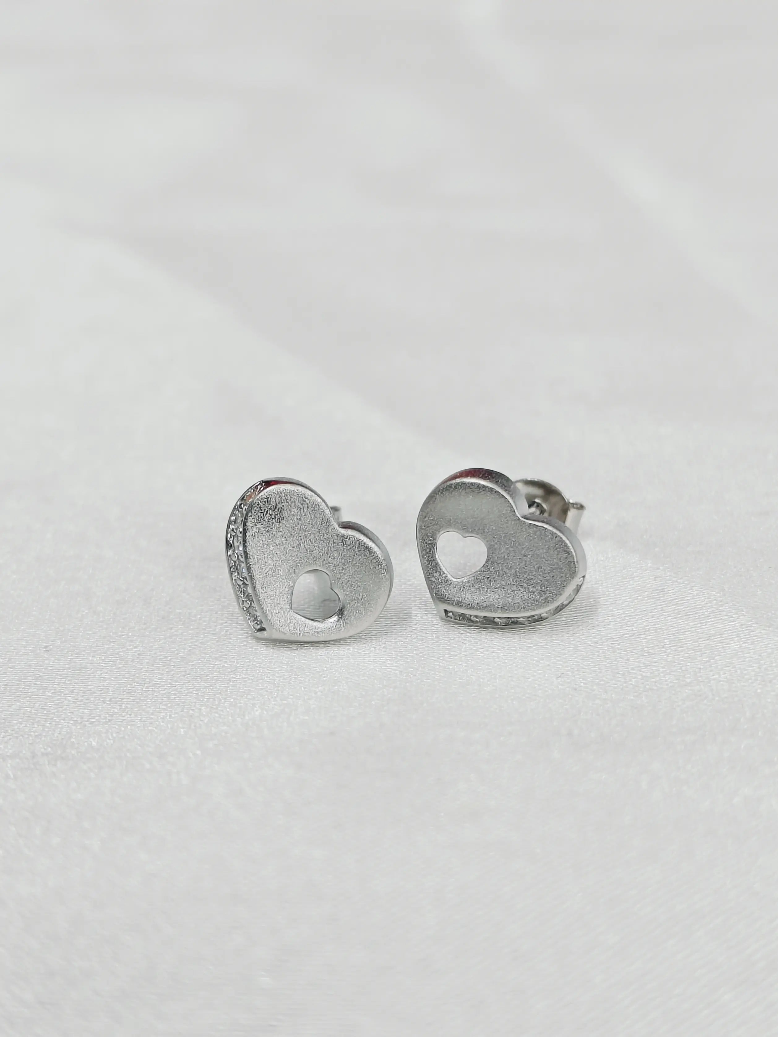 Heart-shaped silver earrings on a light gray background