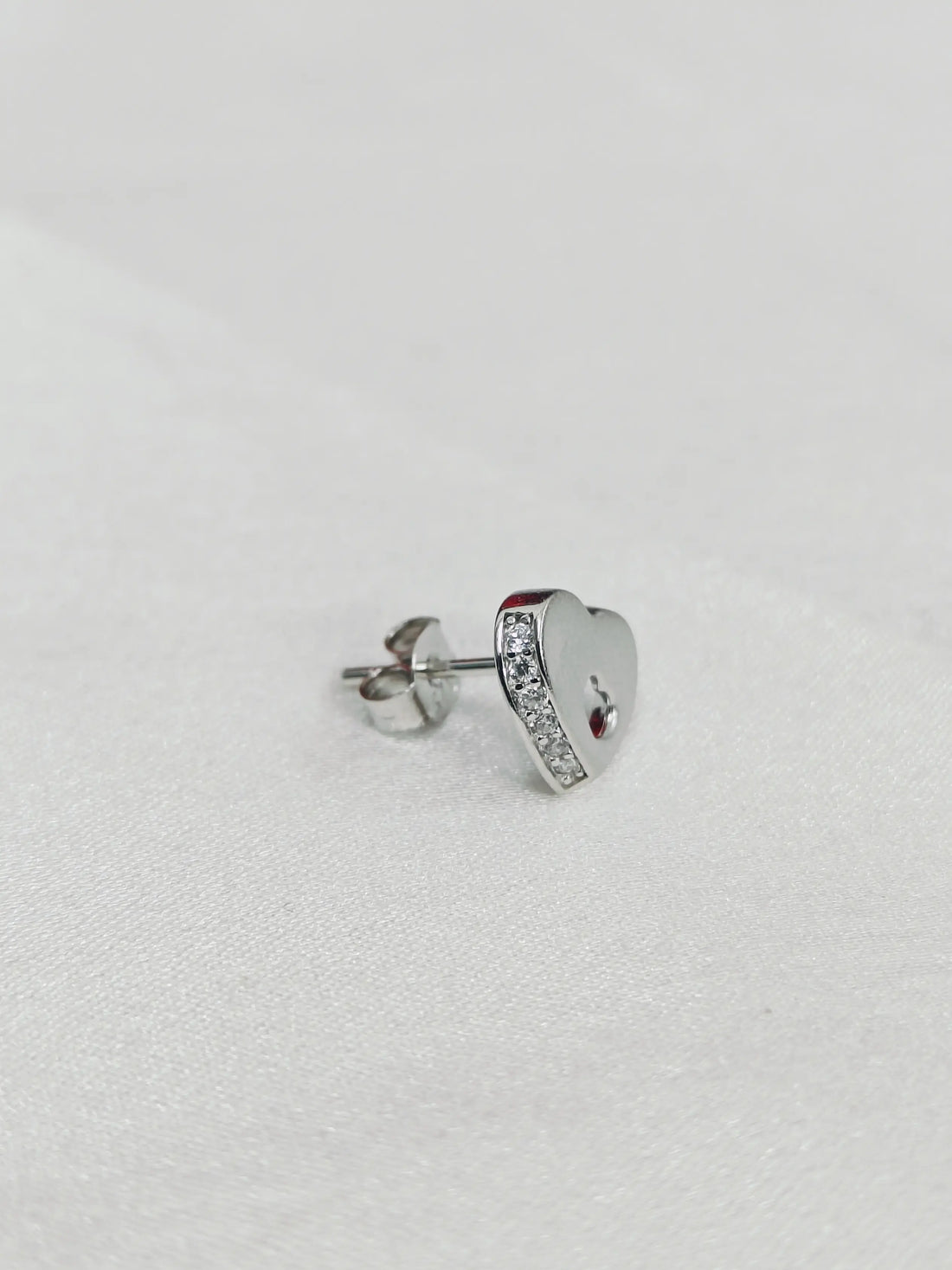 Heart-shaped silver earring with red gemstone on a light gray background