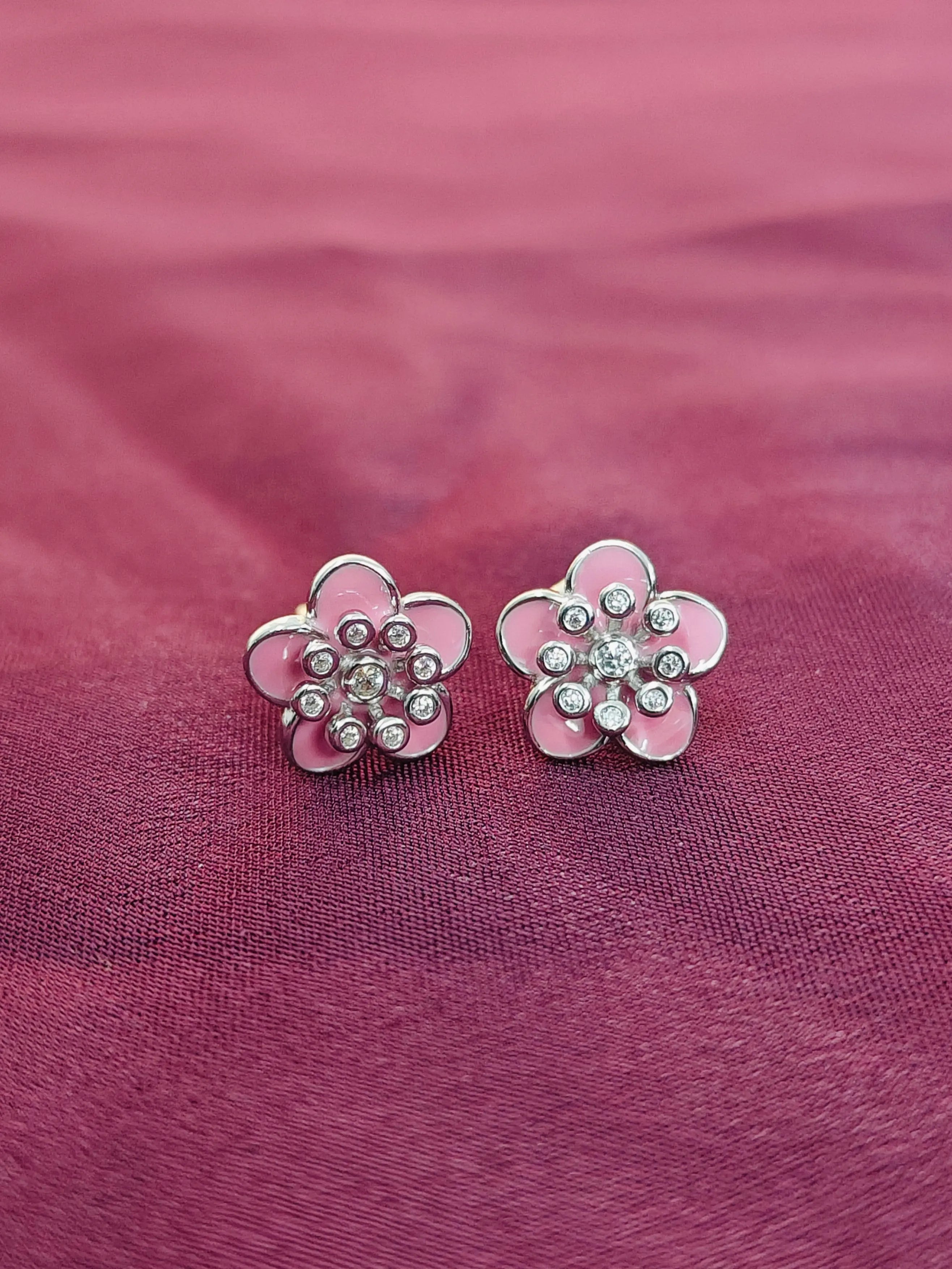 Pink flower-shaped earrings with silver details on a pink fabric background