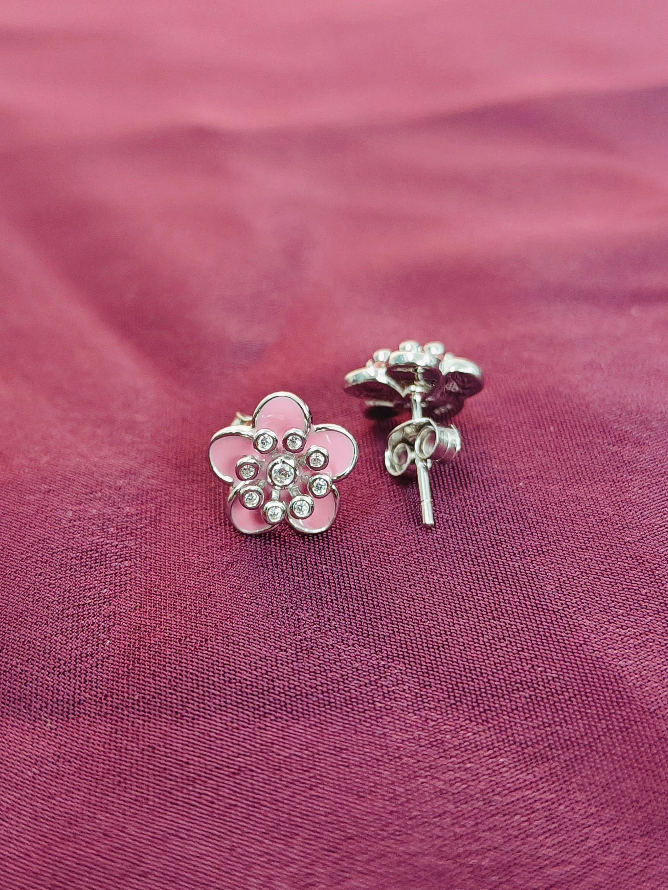 Flower-shaped earrings on a pink fabric background