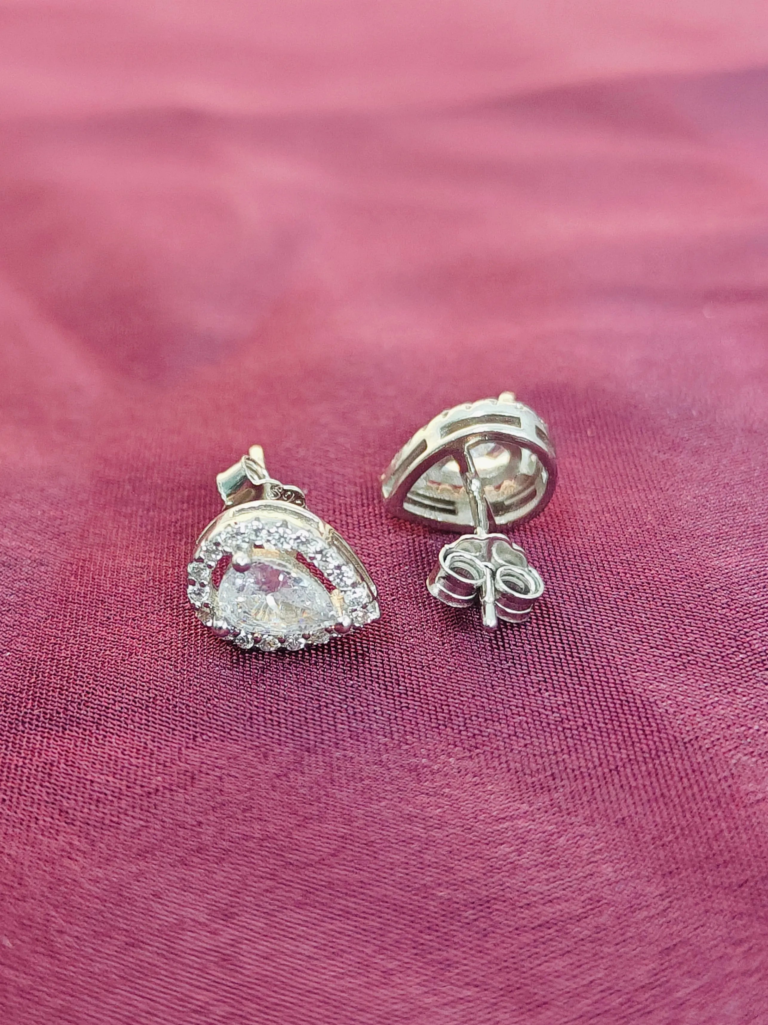 Silver earrings with clear gemstones on a pink fabric background