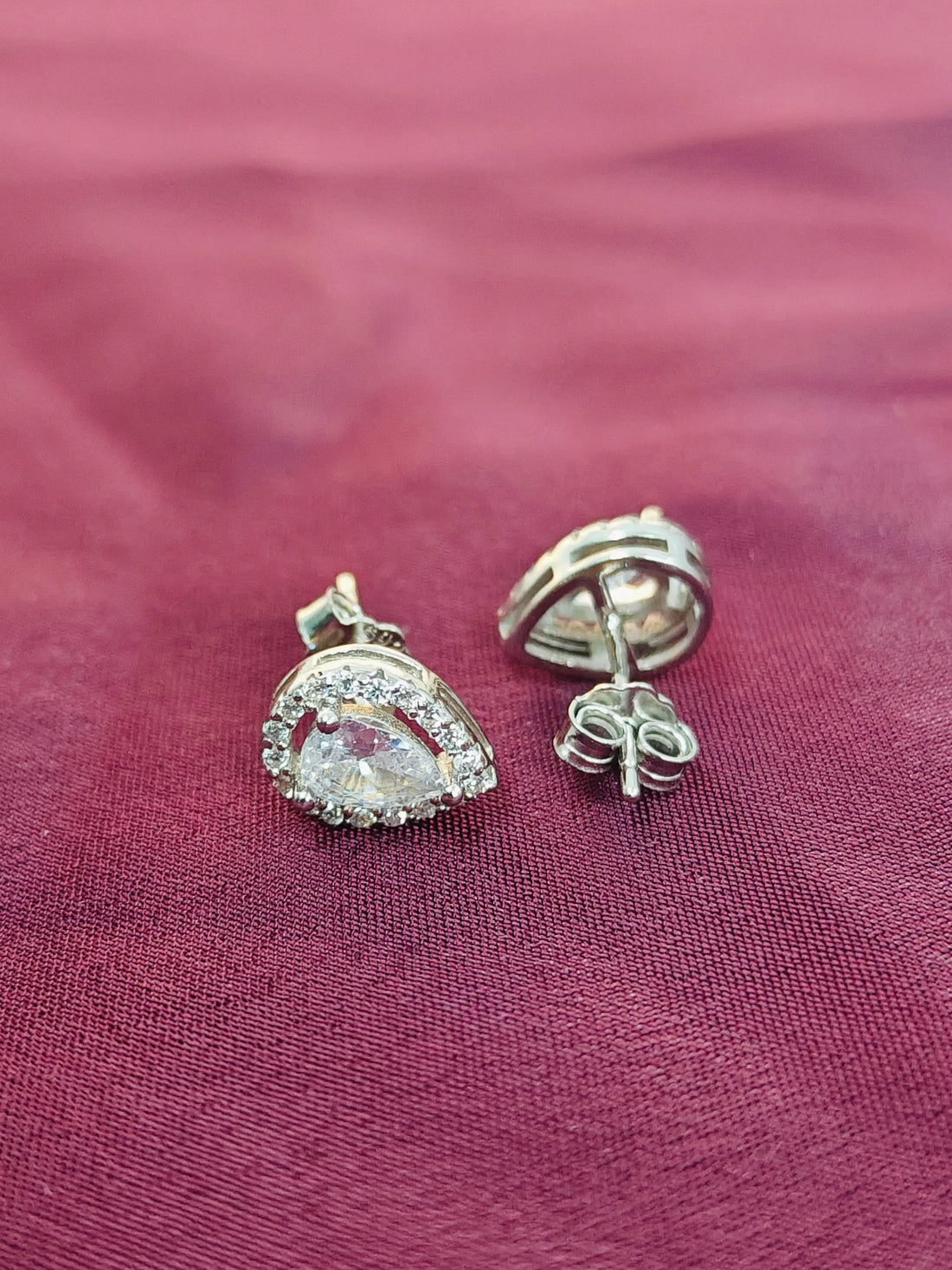 Silver earrings with clear gemstones on a pink fabric background