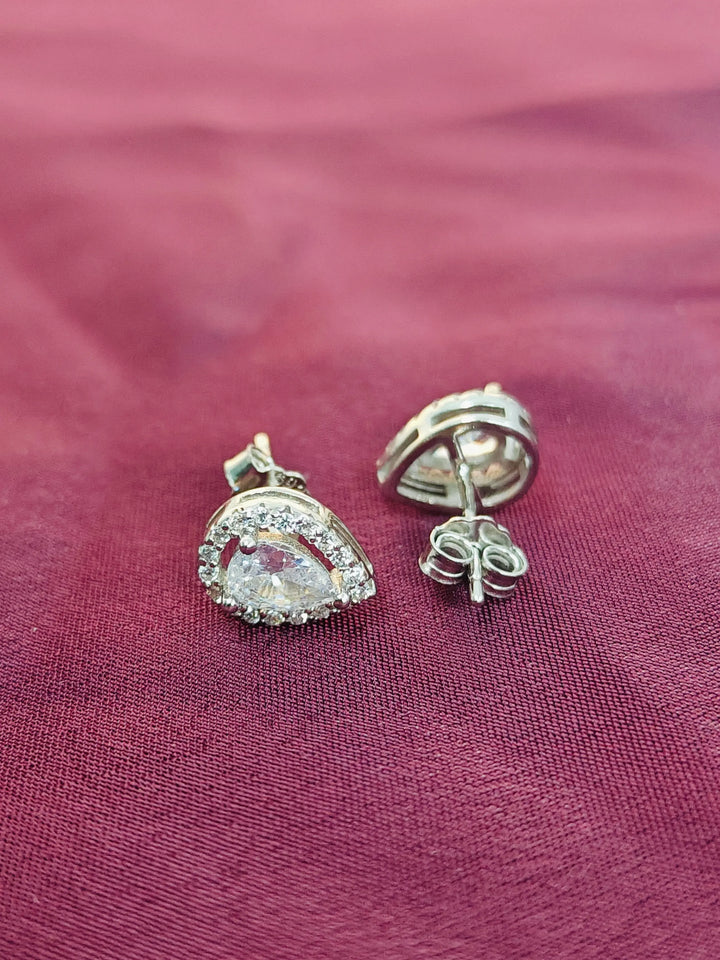 Silver earrings with clear gemstones on a pink fabric background