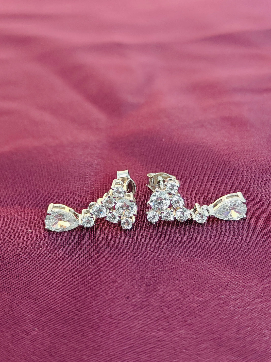 Pair of silver earrings with clear stones on a purple fabric background