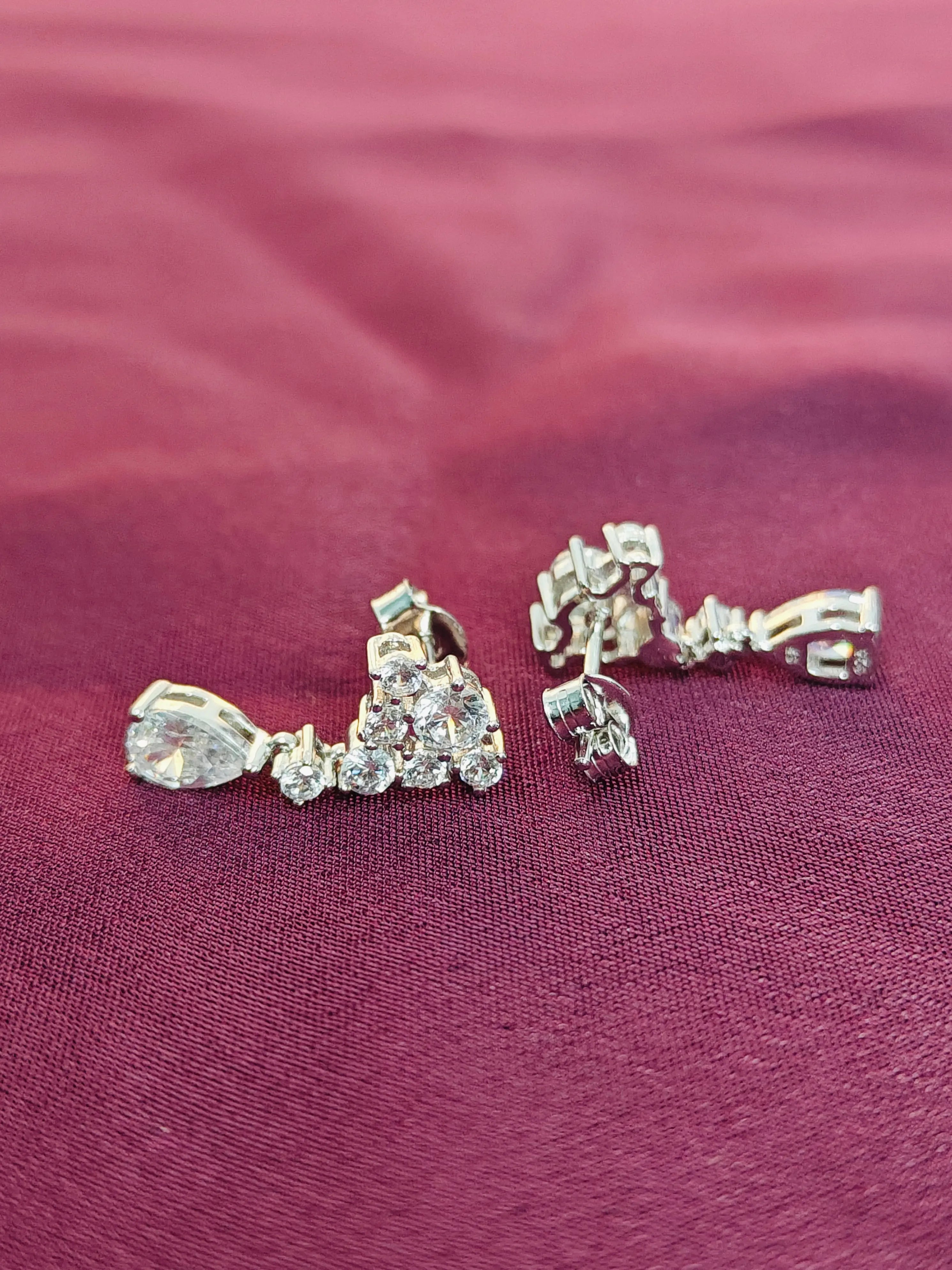 Pair of silver earrings with clear stones on a pink fabric background