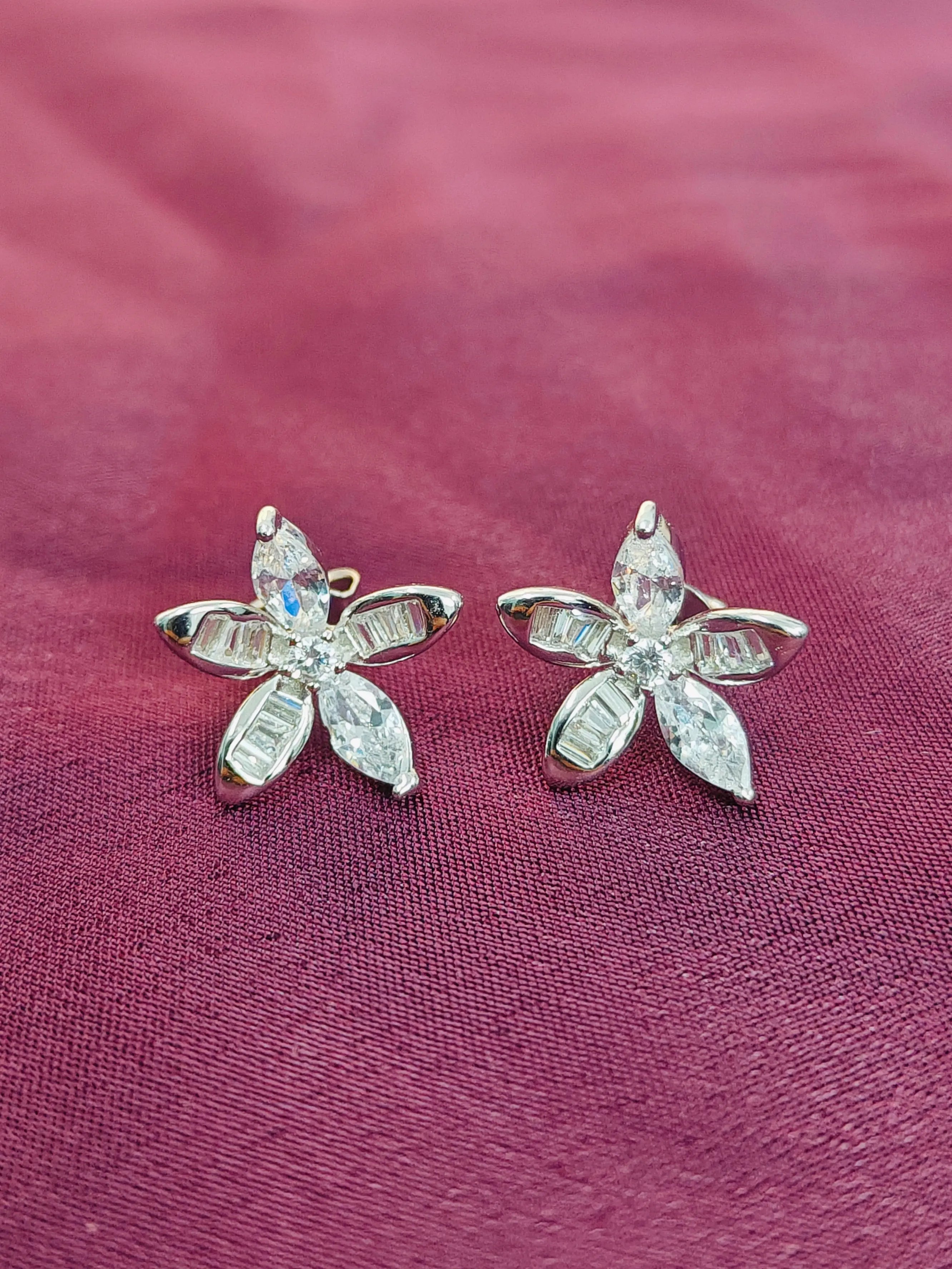 Flower-shaped earrings with clear stones on a pink fabric background