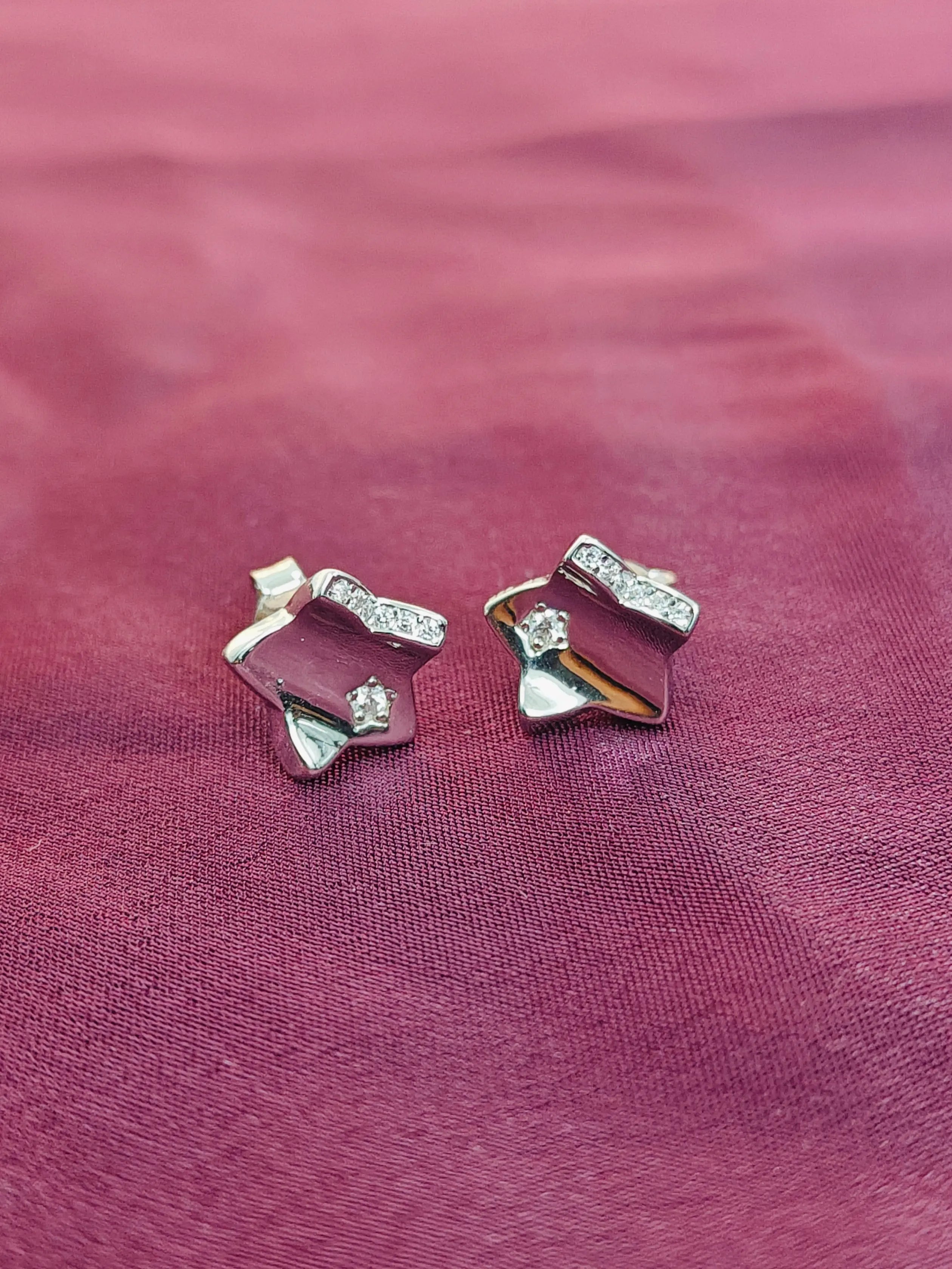 Pair of silver earrings with gemstones on a pink fabric background