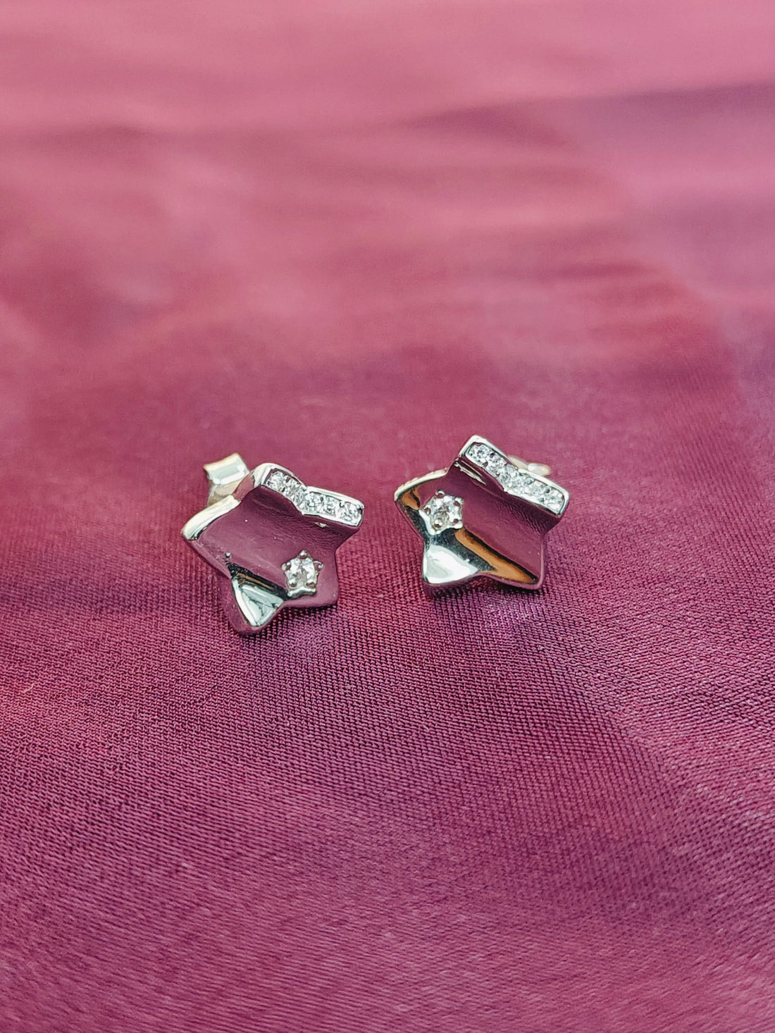 Pair of silver earrings with gemstones on a pink fabric background