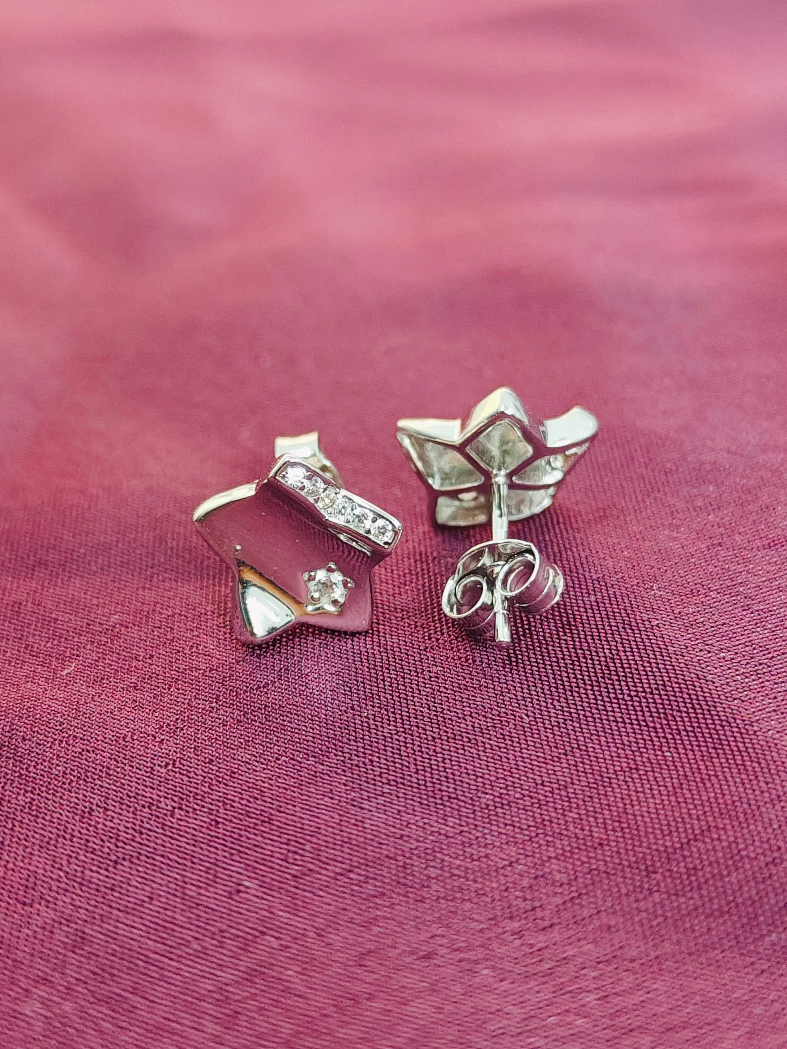 Pair of silver earrings with bow and heart designs on a pink fabric background