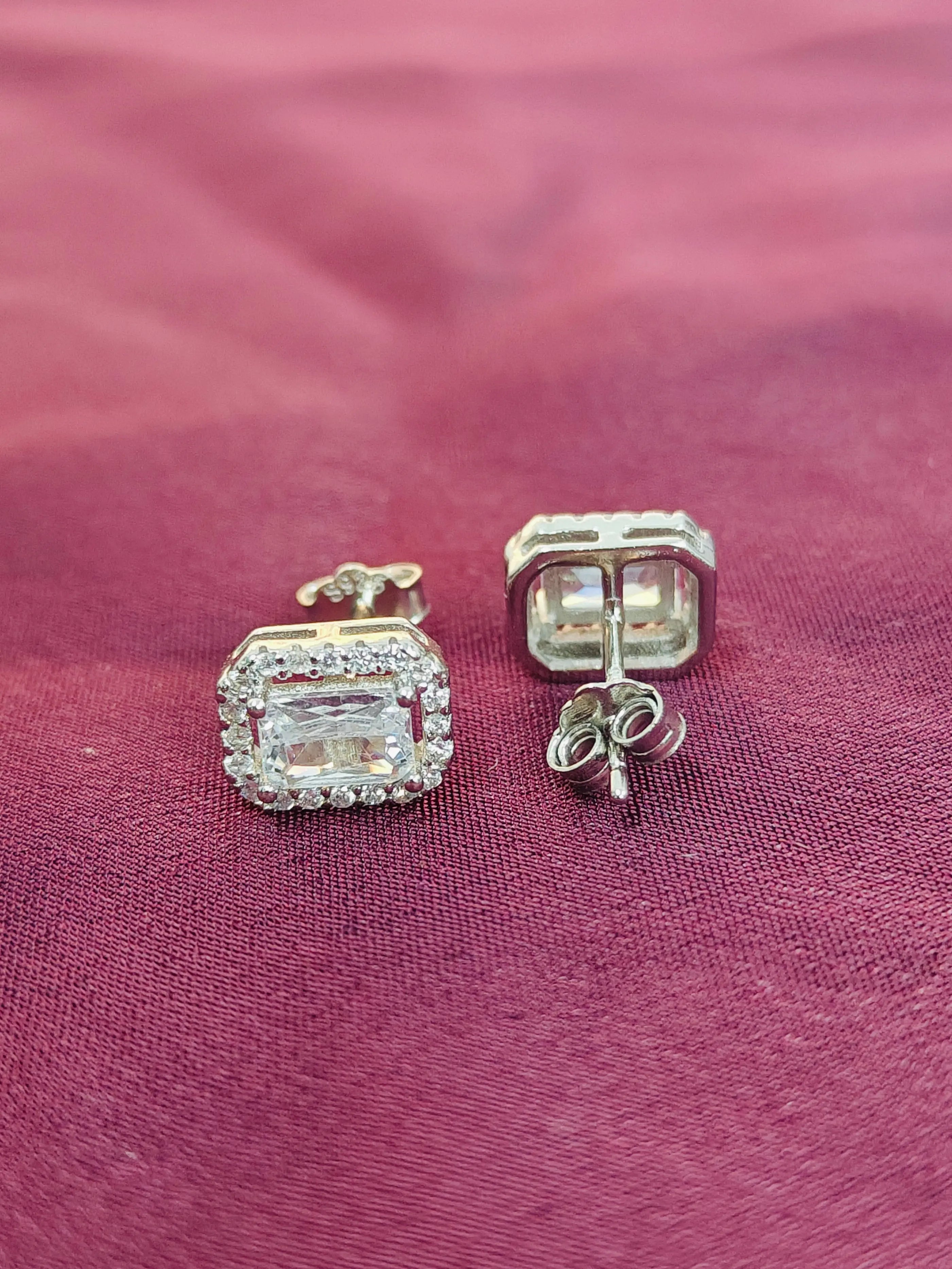 Pair of silver earrings with gemstones on a pink fabric background