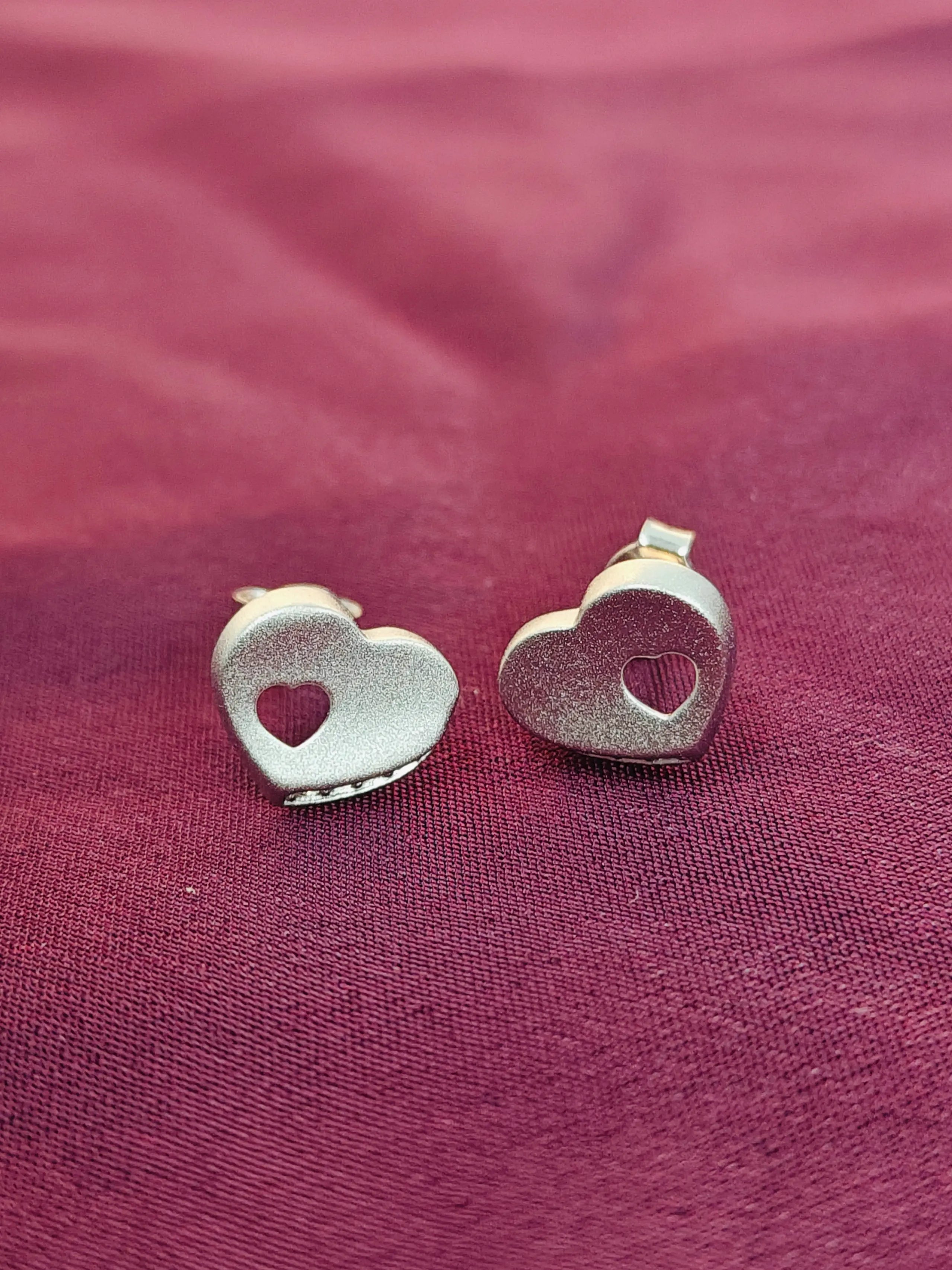 Heart-shaped silver earrings on a red fabric background