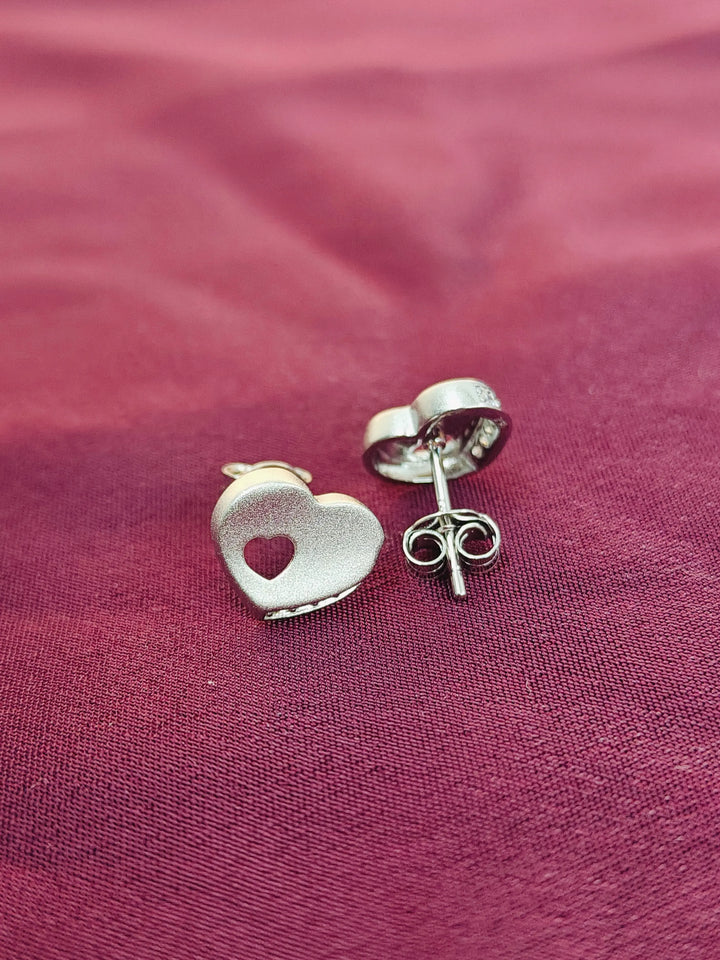 Silver heart-shaped earrings on a pink fabric background