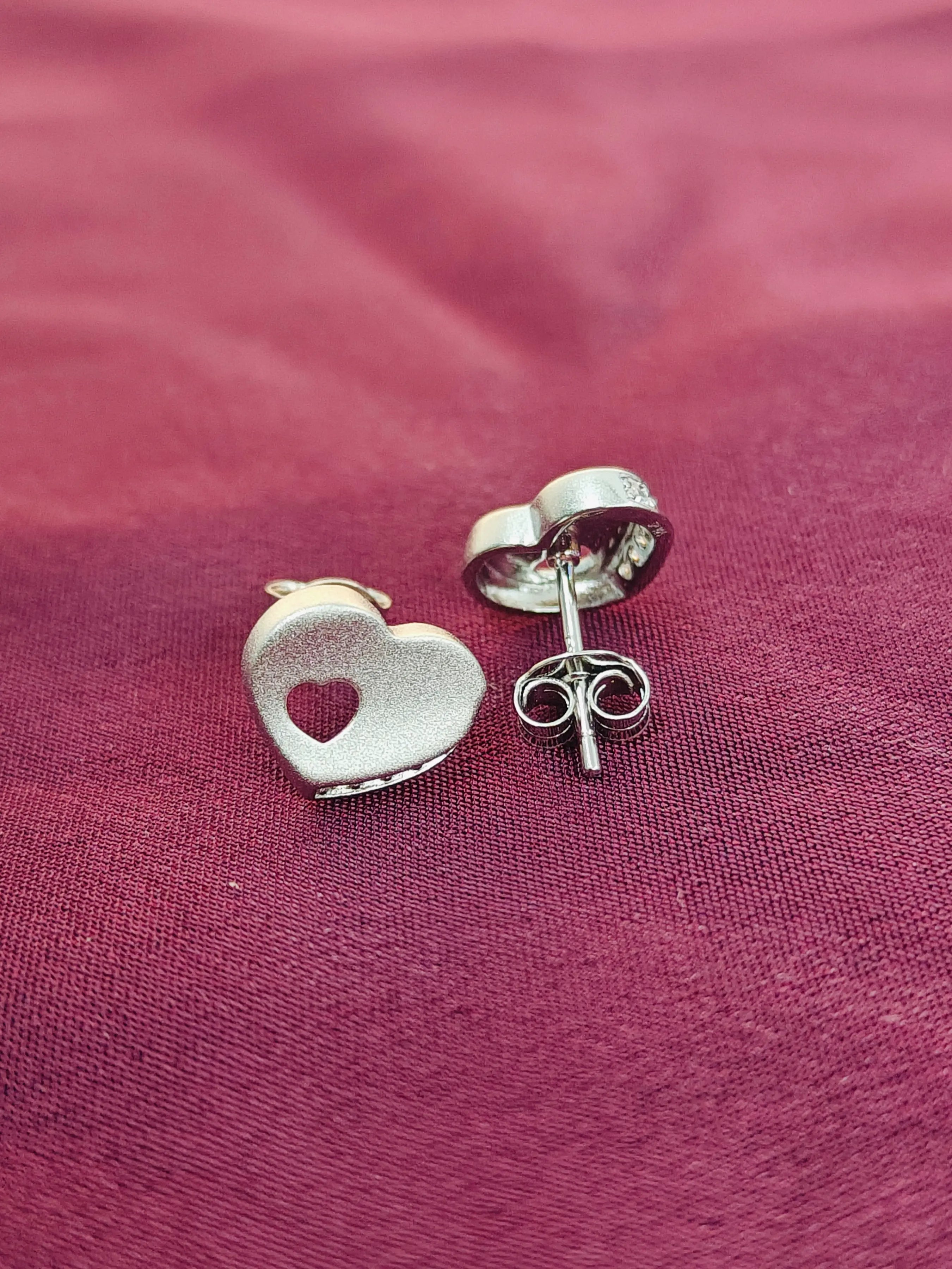 Silver heart-shaped earrings on a pink fabric background