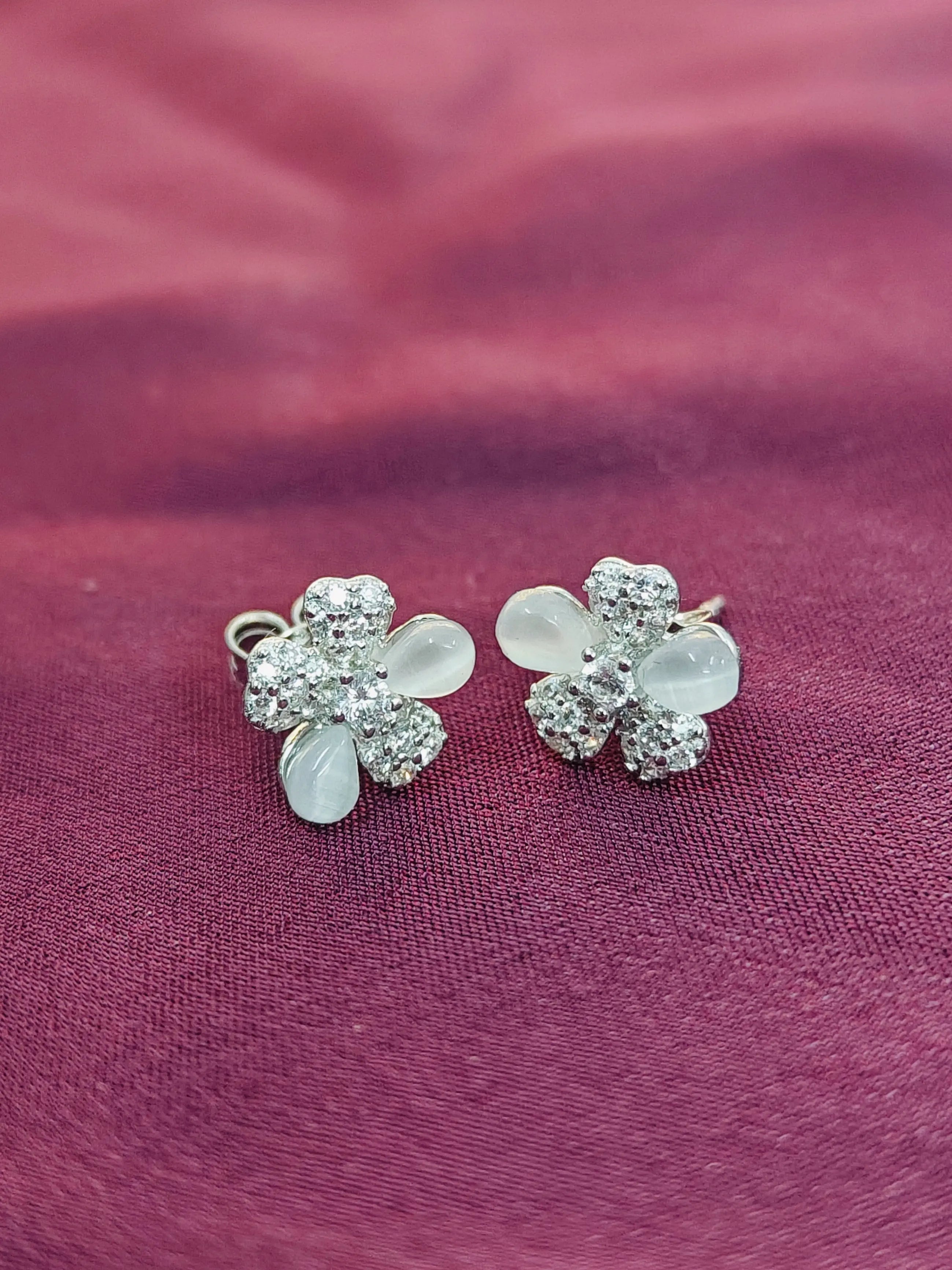 Flower-shaped earrings with clear stones on a purple fabric background