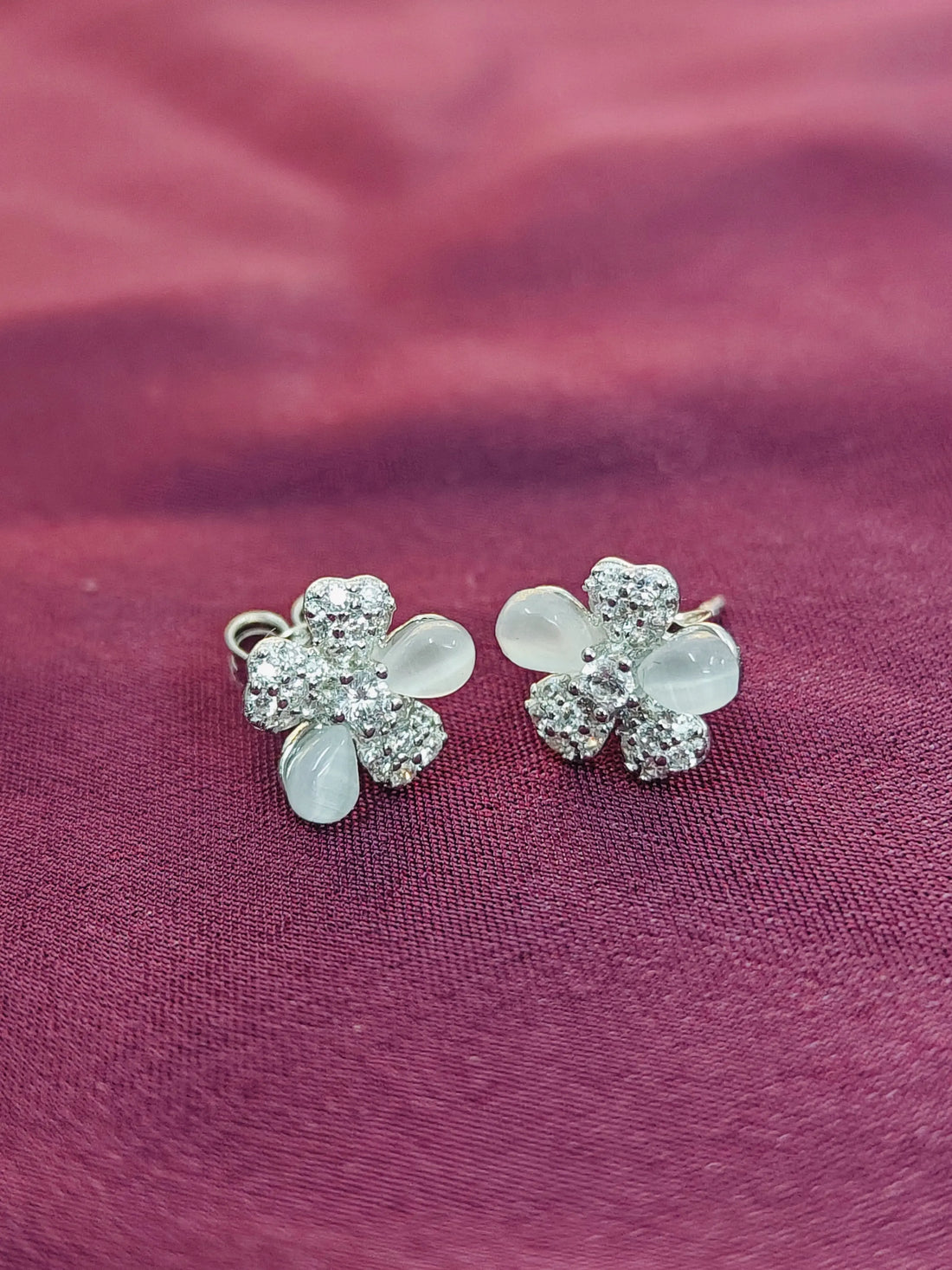 Flower-shaped earrings with clear stones on a purple fabric background