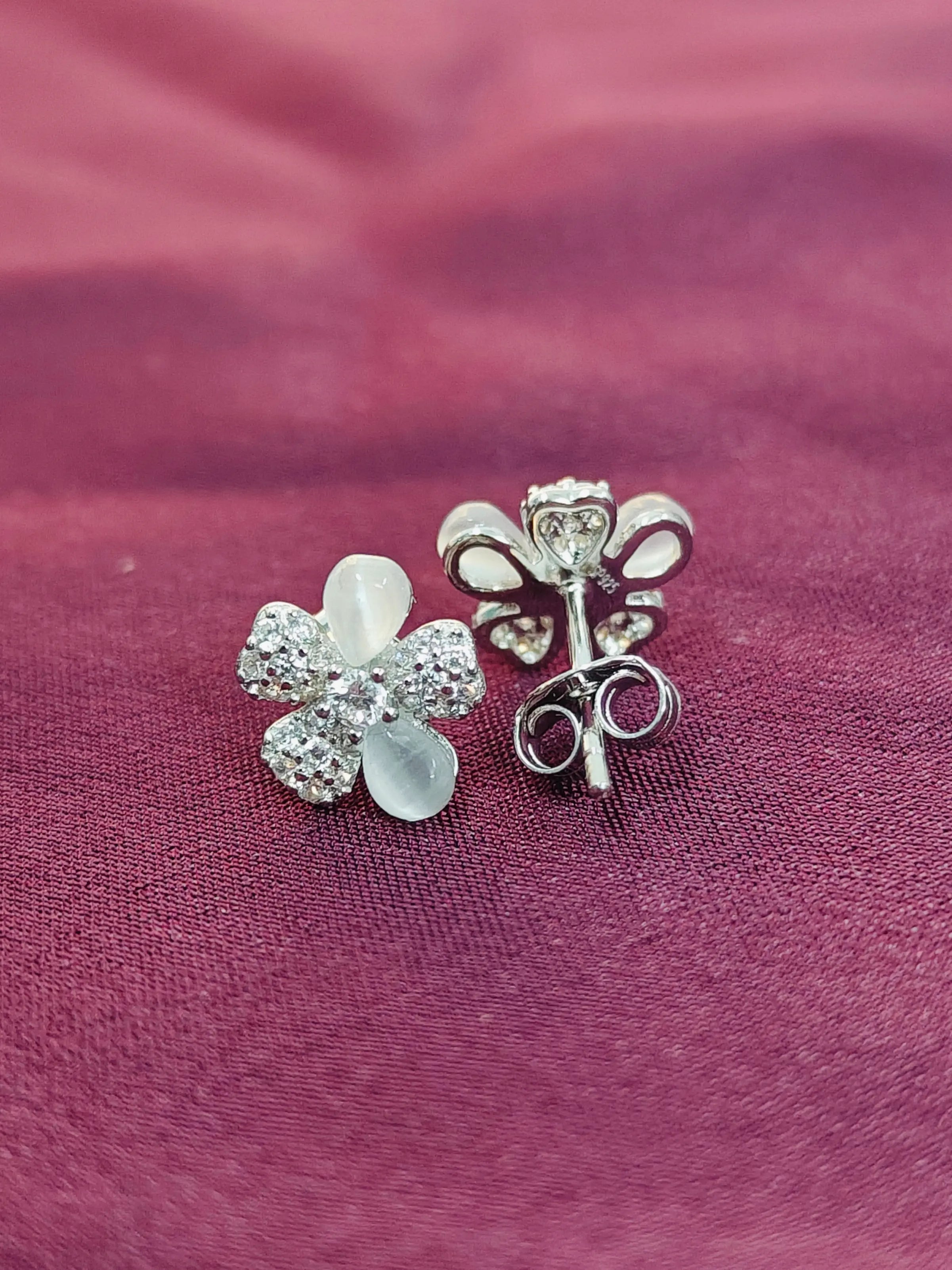 Silver flower-shaped earrings on a purple fabric background