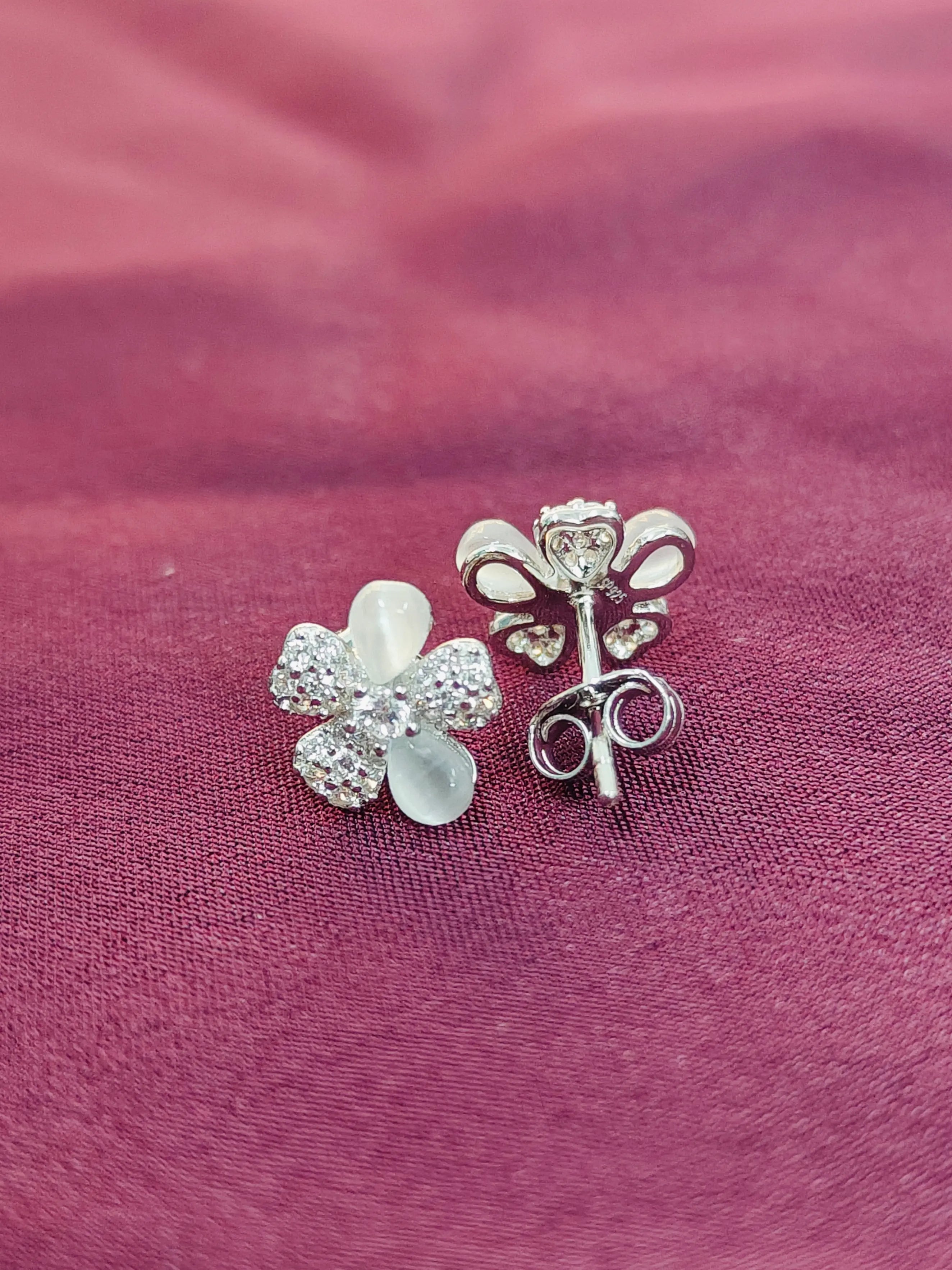 Two silver floral earrings on a pink fabric background