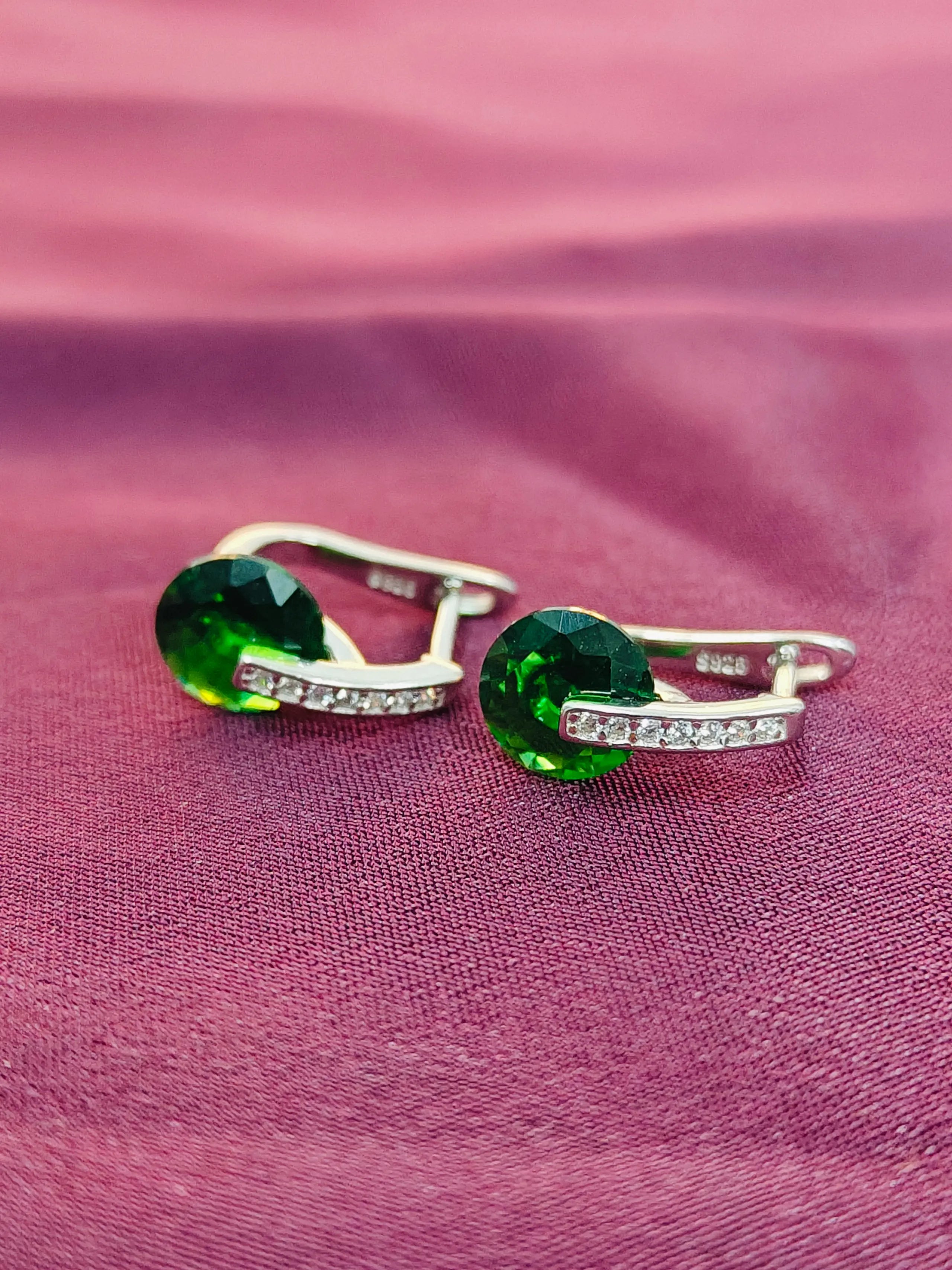 Green gemstone earrings on a pink fabric background