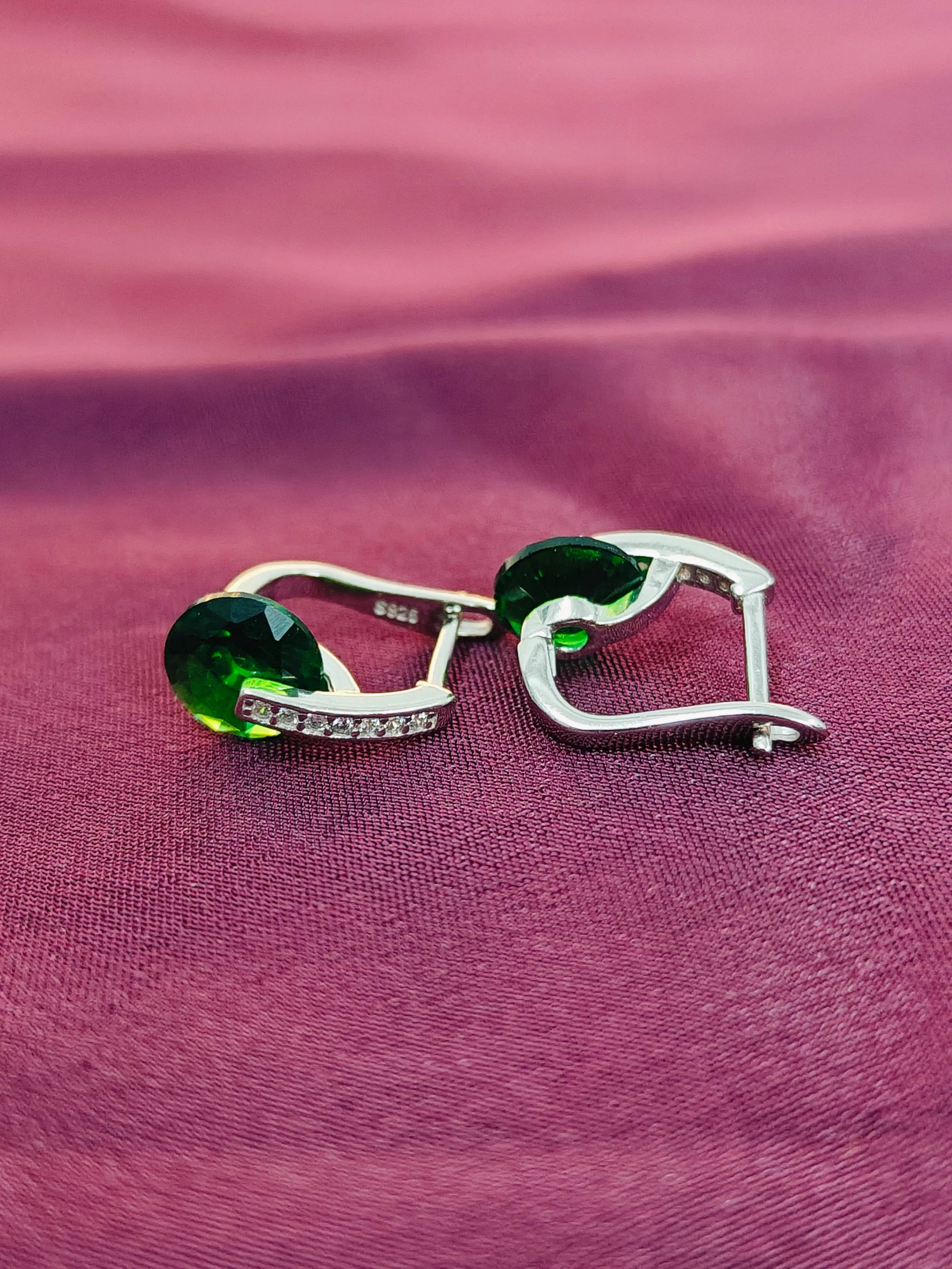 Pair of earrings with green gemstones on a purple fabric background