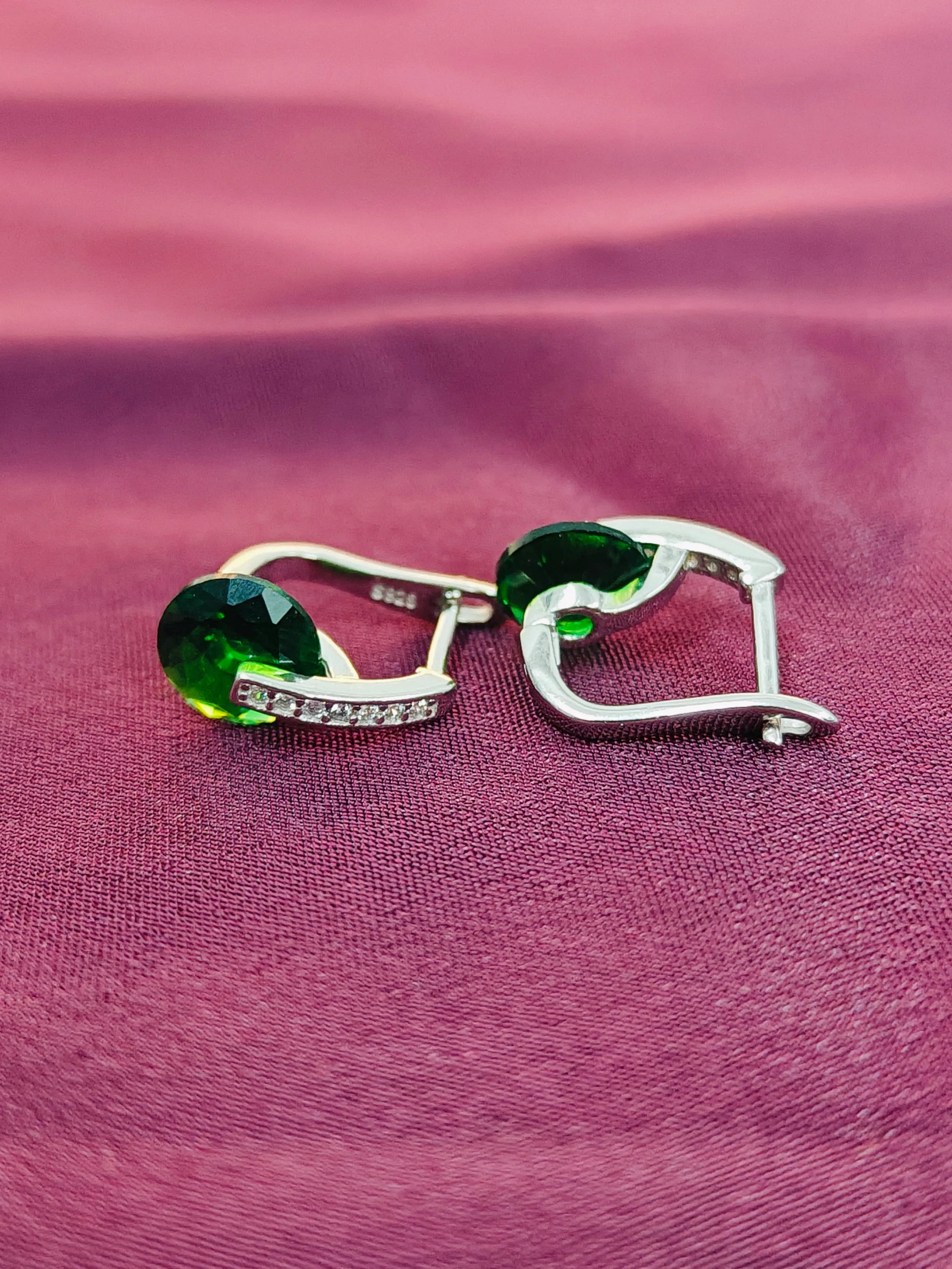 Heart-shaped earrings with green gemstones on a pink fabric background