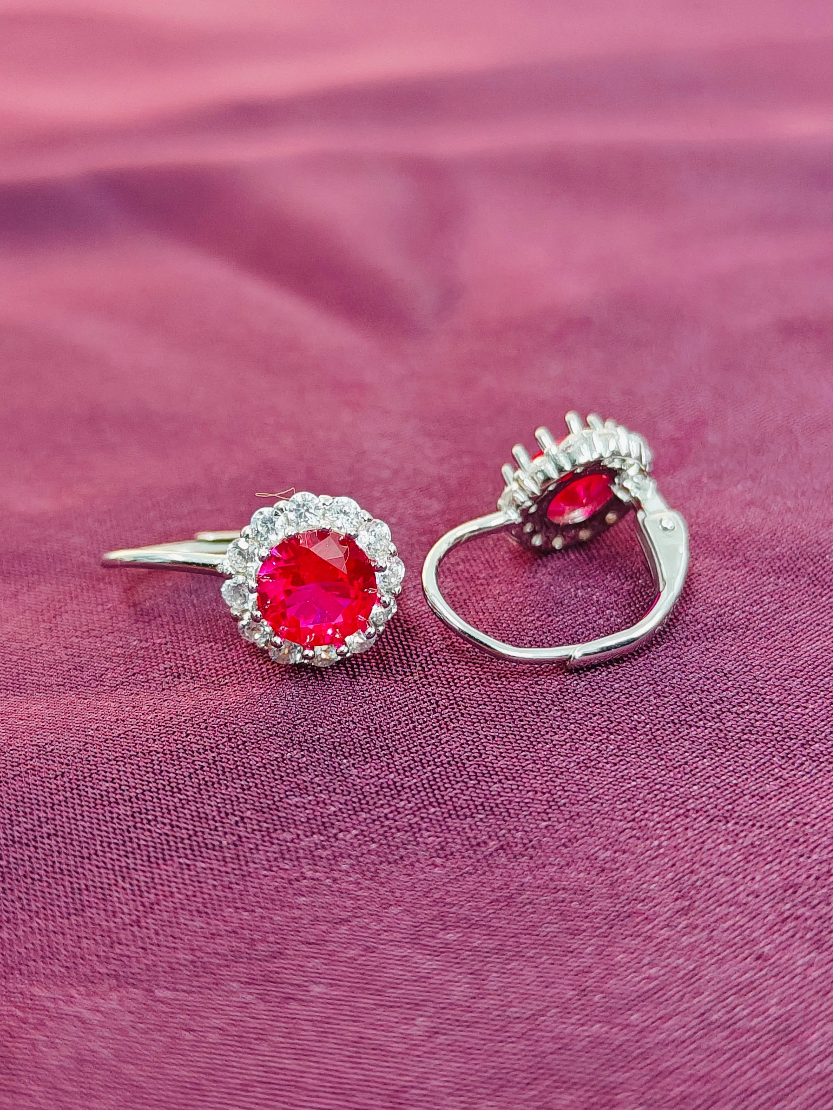 Pair of earrings with red gemstones on a pink fabric background