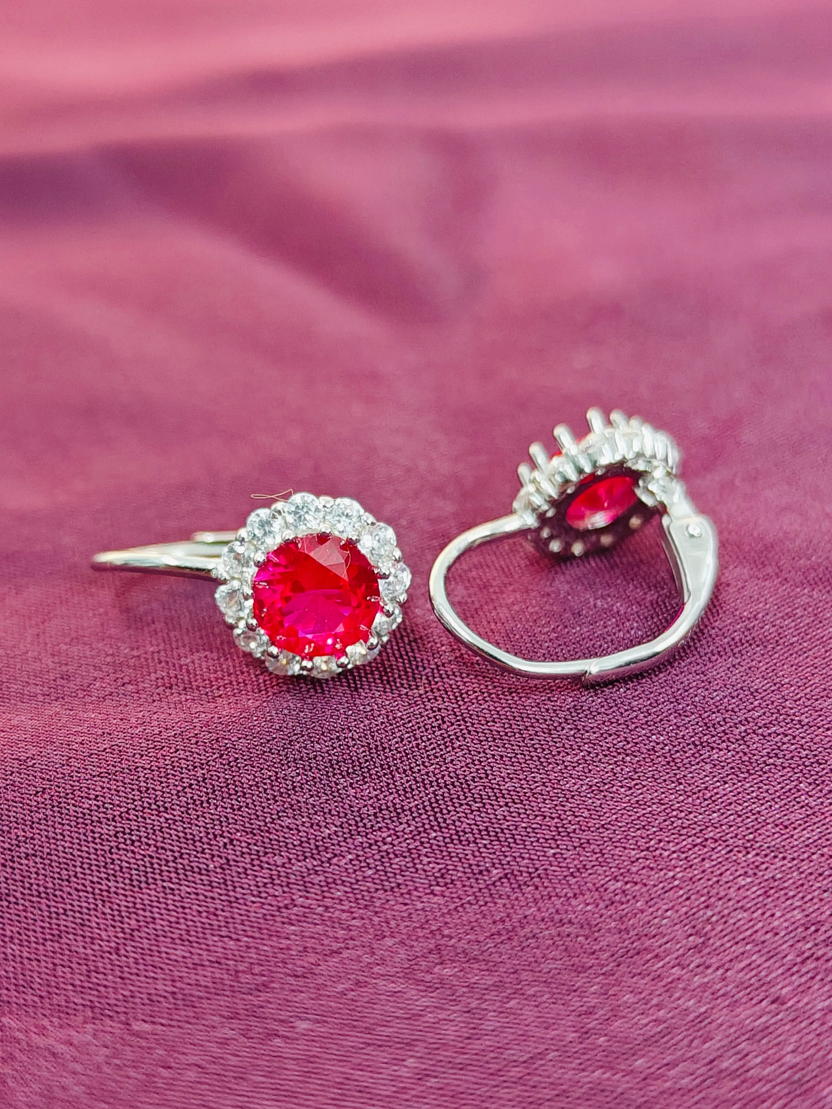 Two silver rings with red gemstones on a pink fabric background