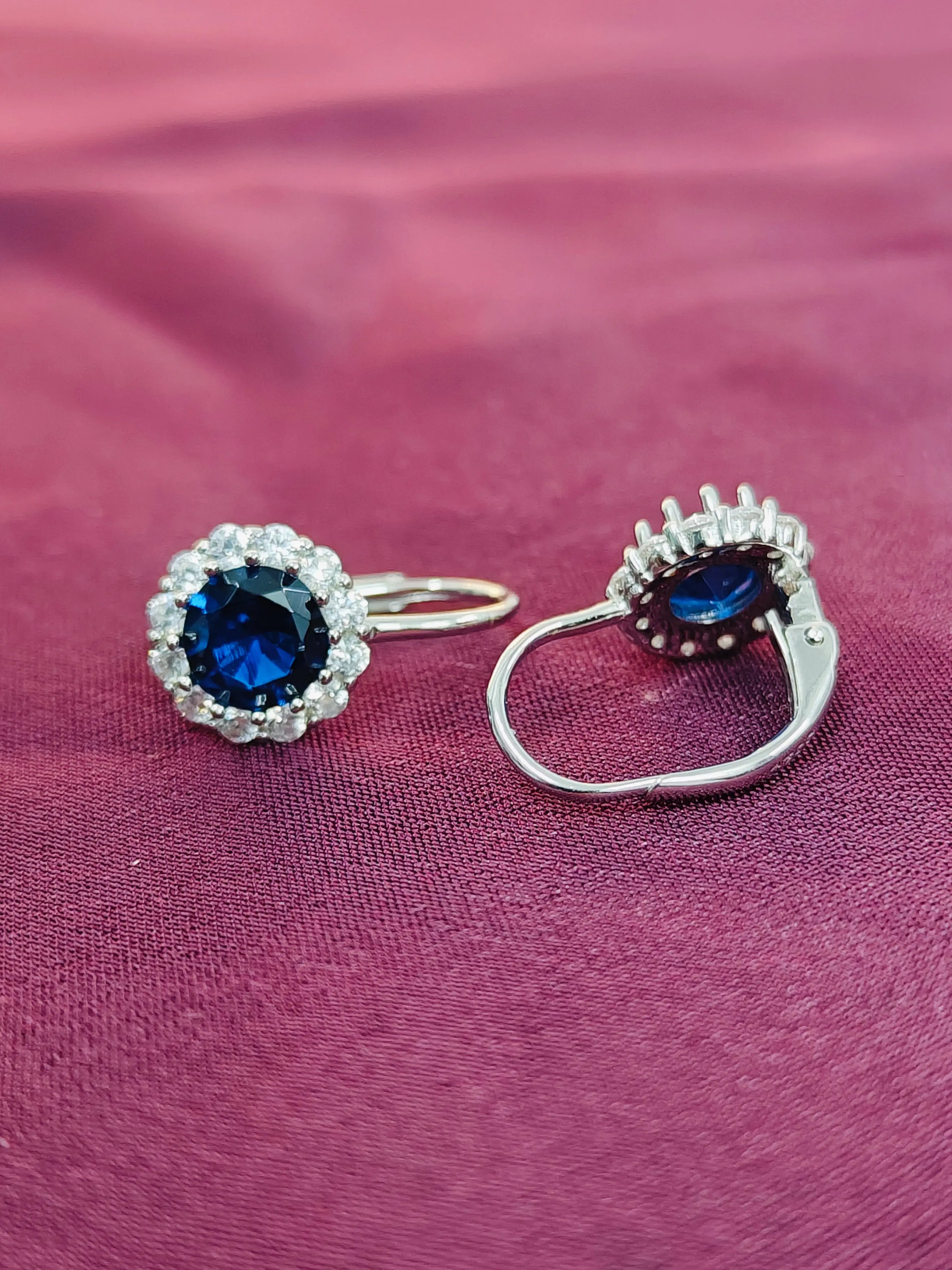 Silver earrings with blue gemstones on a pink fabric background