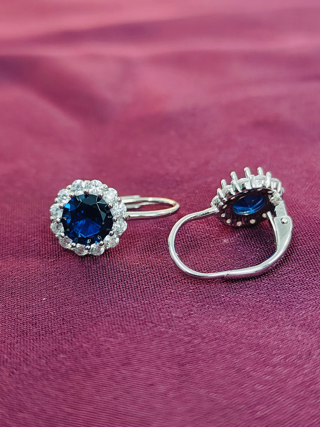 Silver earrings with blue gemstones on a purple fabric background