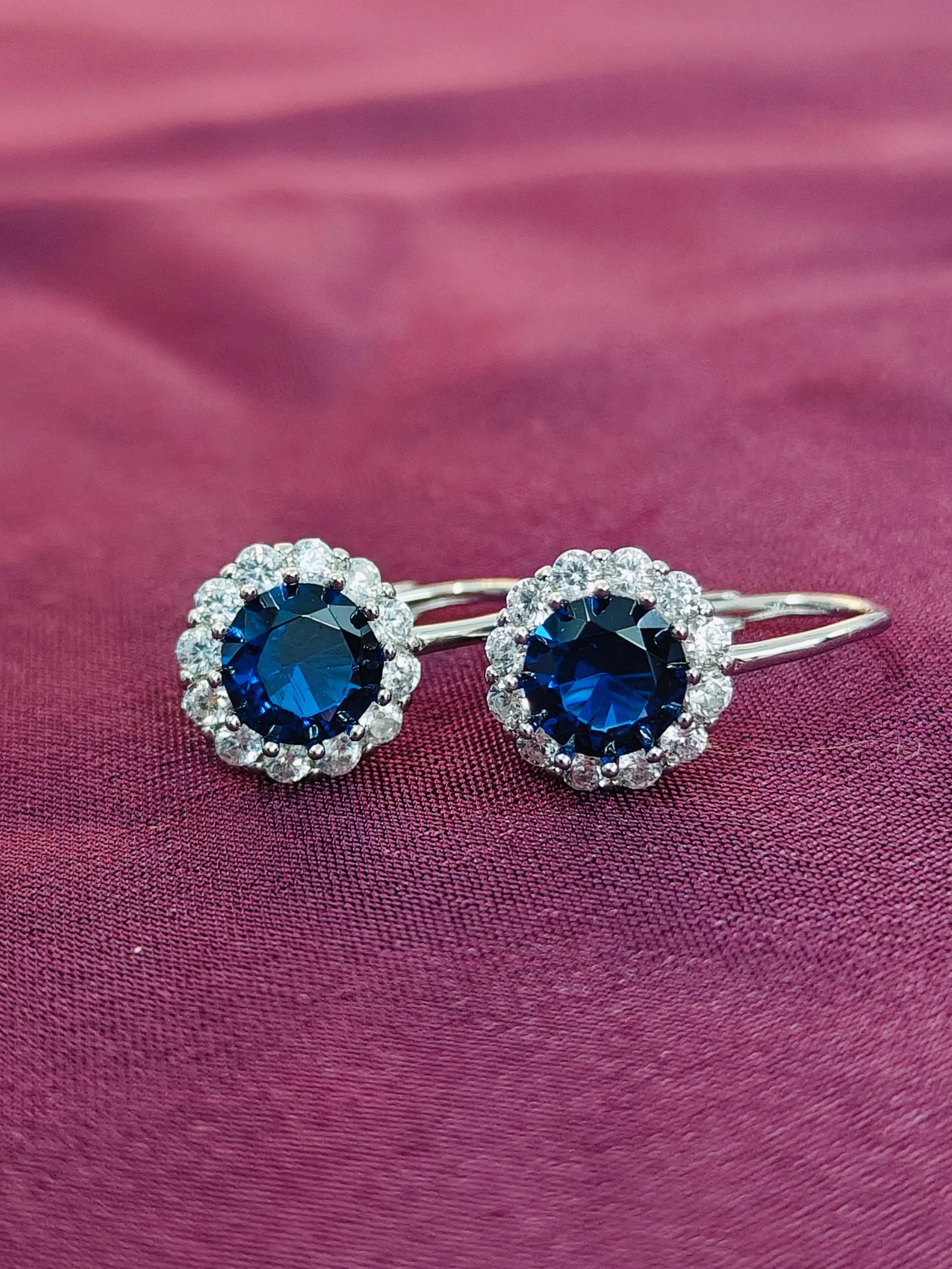 Pair of silver hair clips with blue gemstones on a pink fabric background