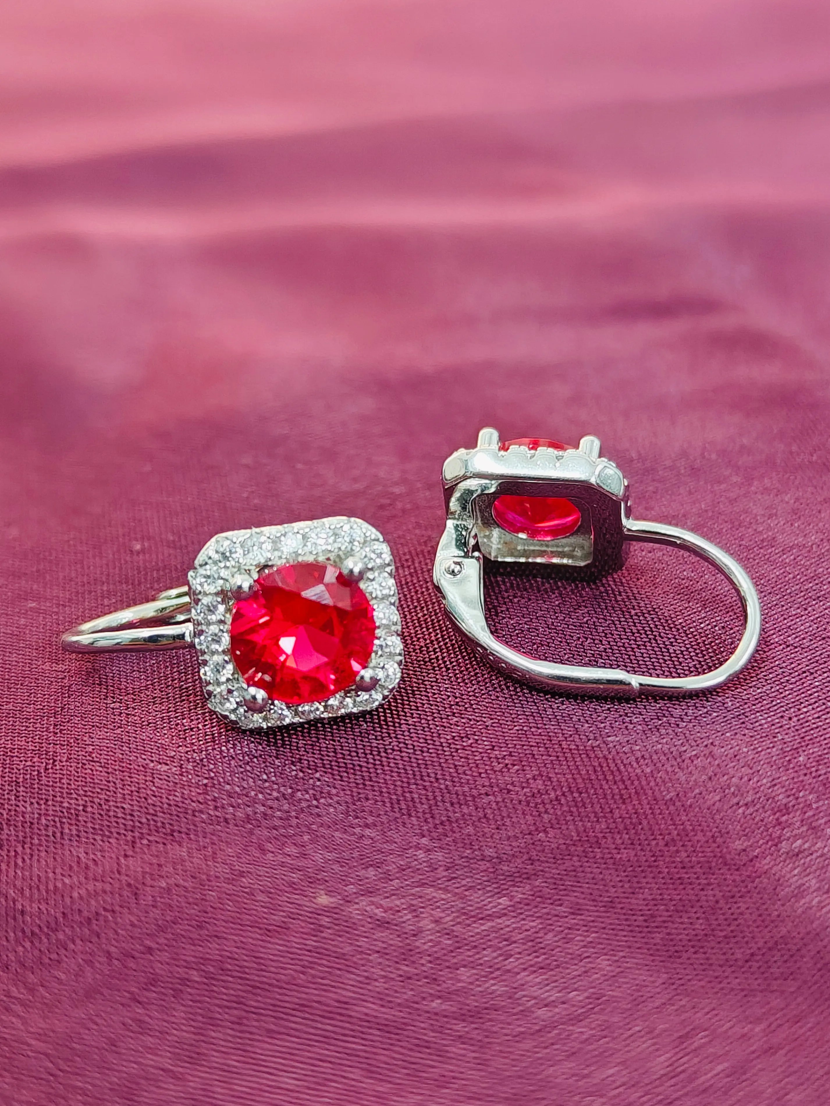 Pair of earrings with red gemstones on a pink fabric background