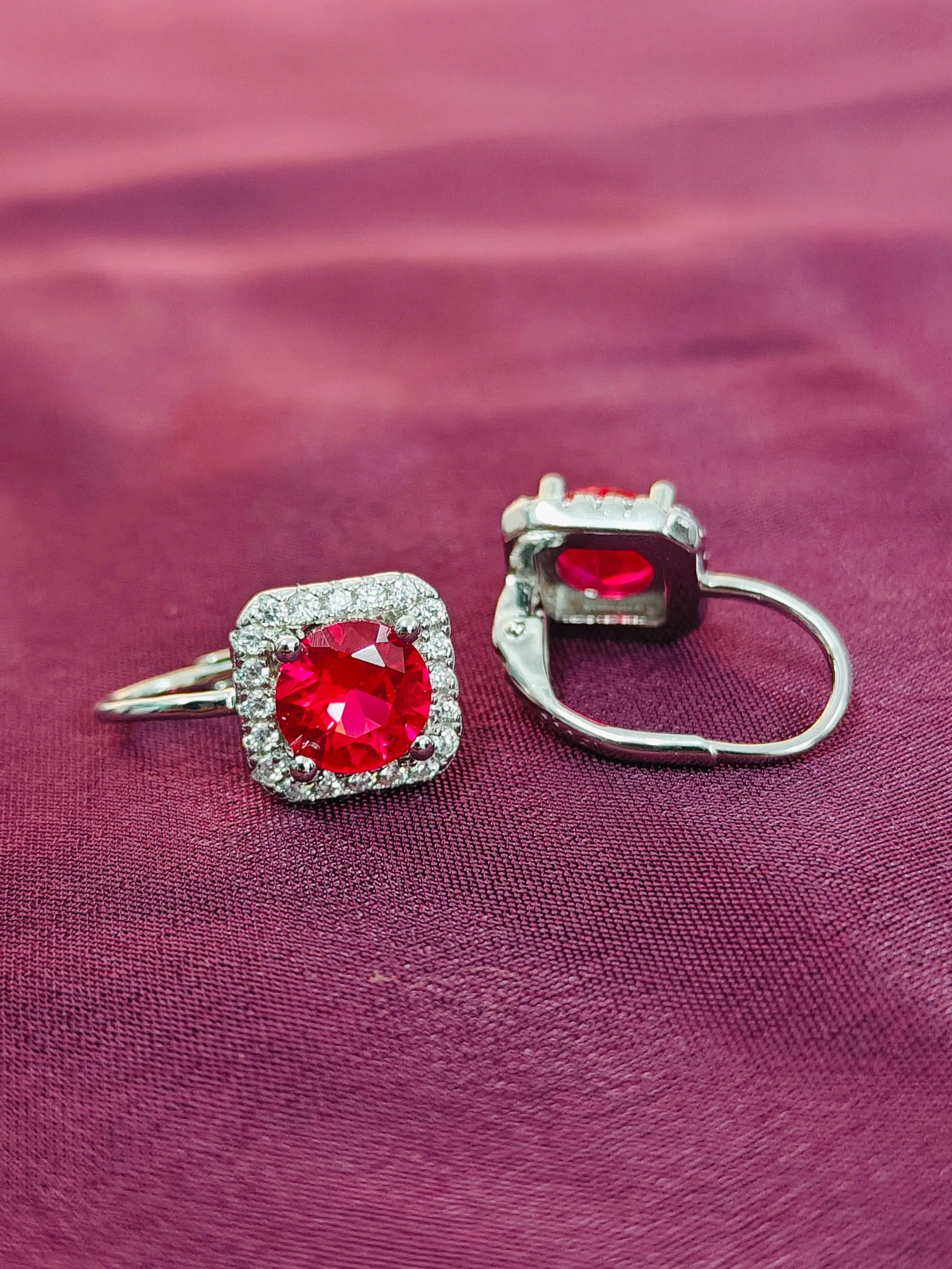 Pair of earrings with red gemstones on a purple fabric background