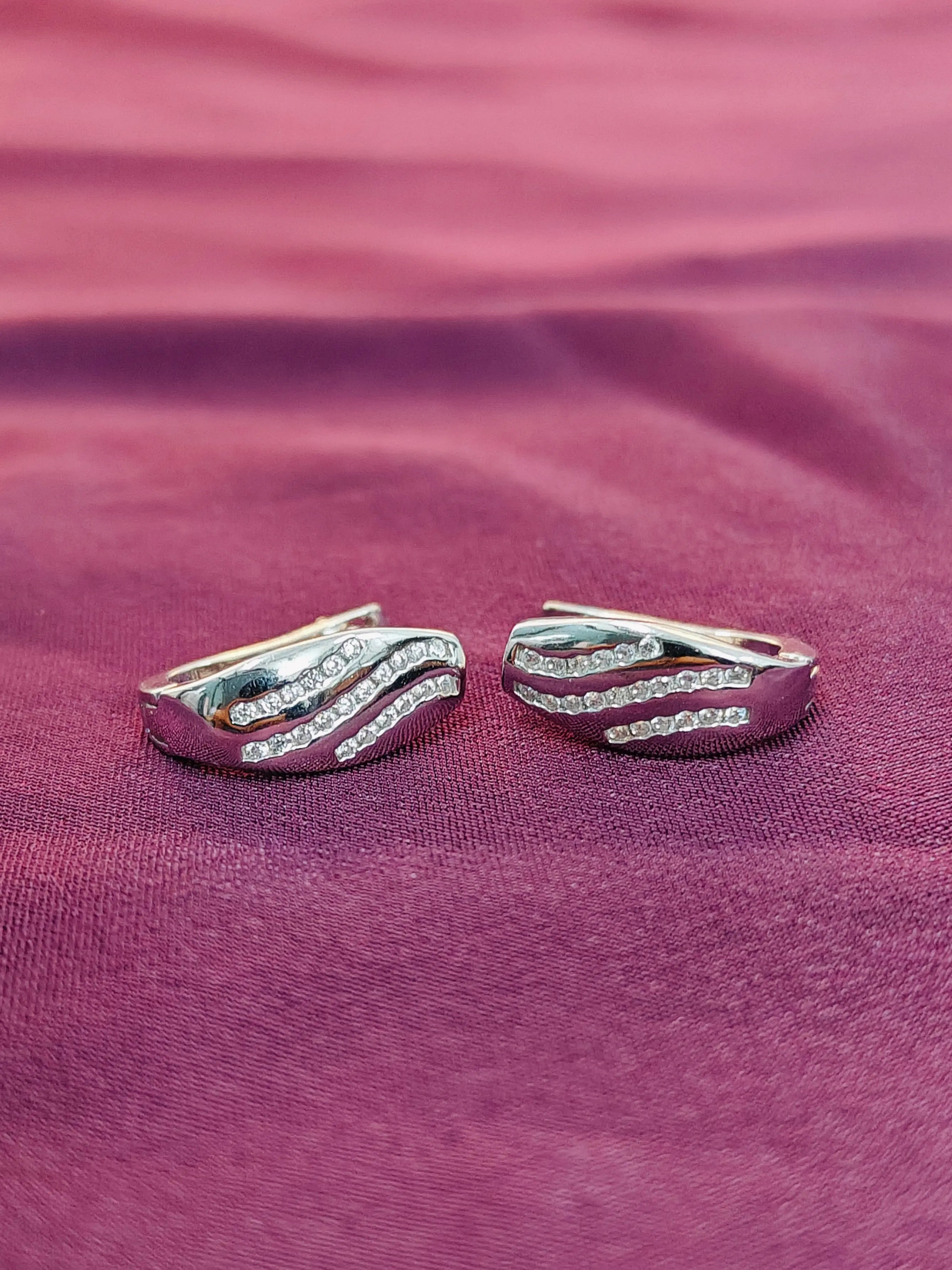 Pair of silver hoop earrings with clear stones on a purple fabric background