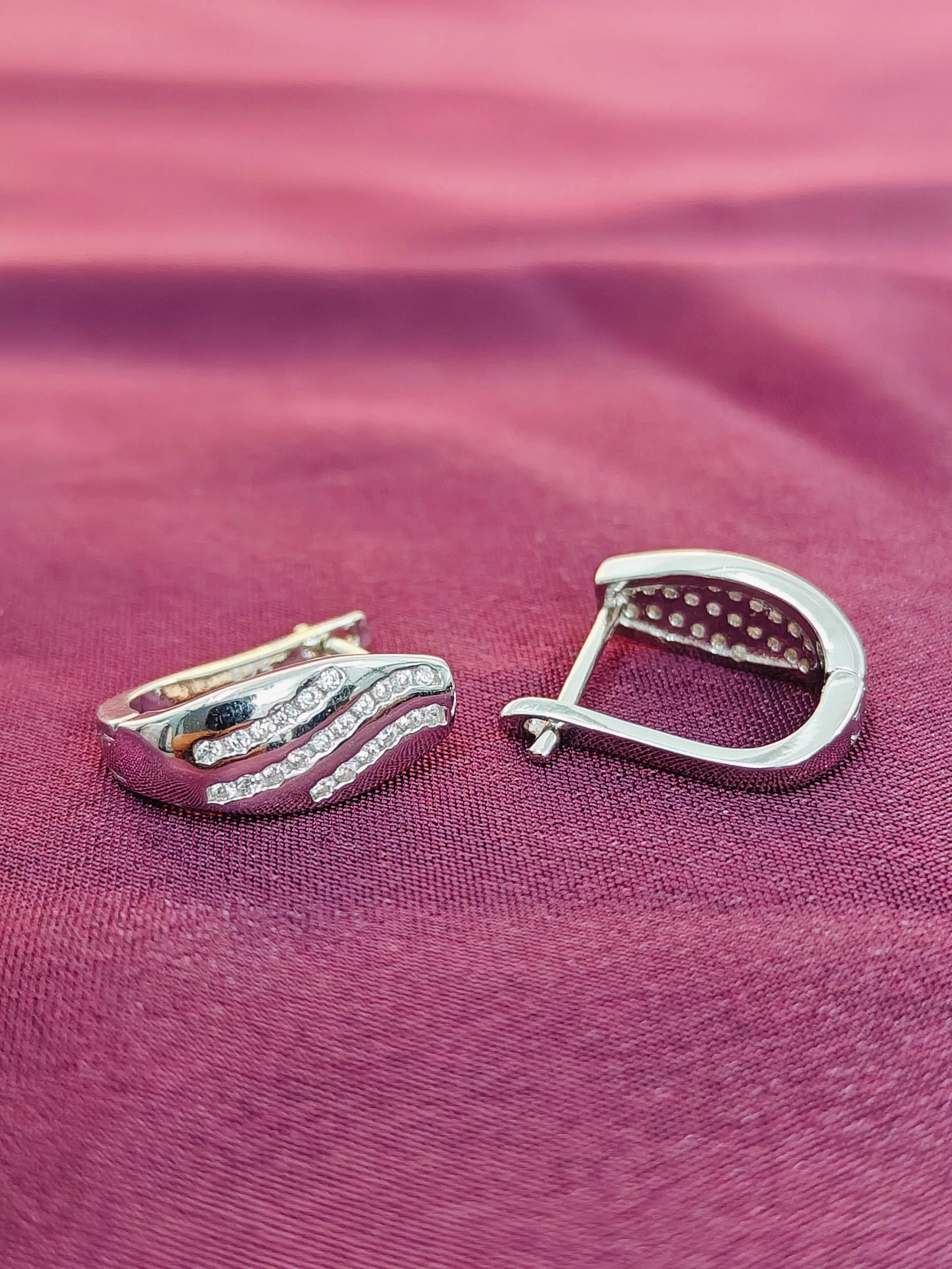 Silver earring on a pink fabric background