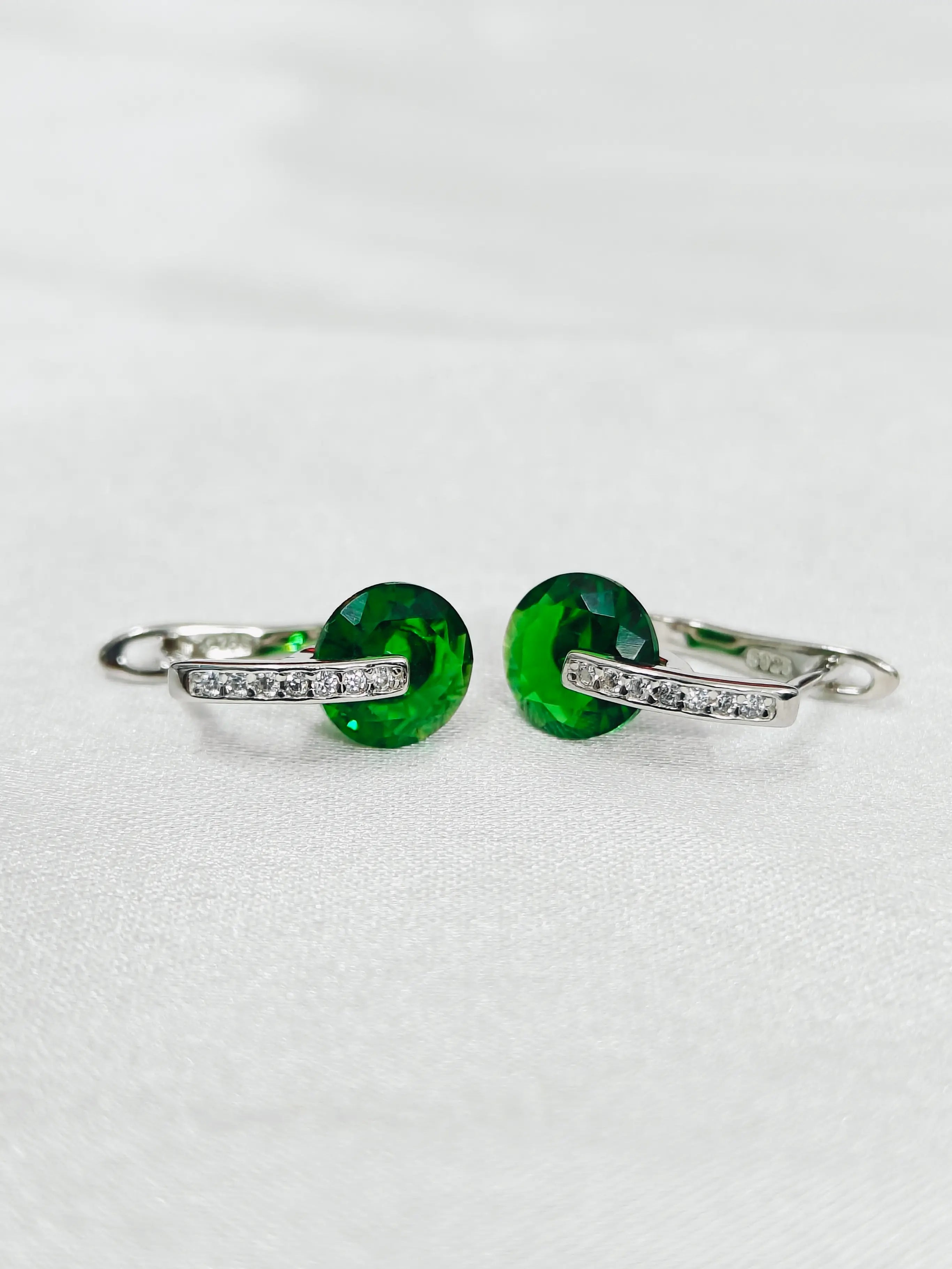 Pair of hoop earrings with green gemstones on a light gray background