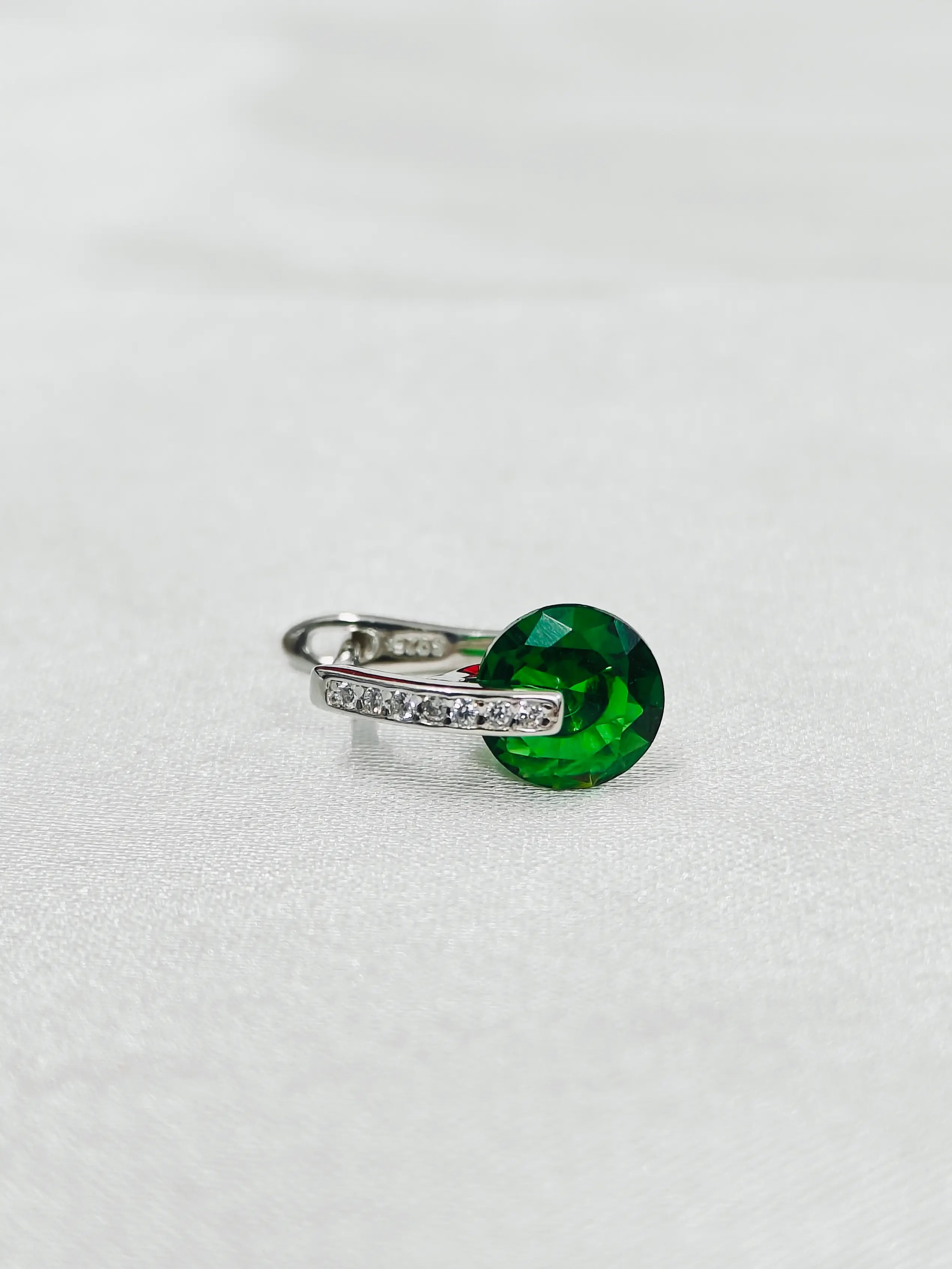Ring with a green gemstone and silver band on a white background