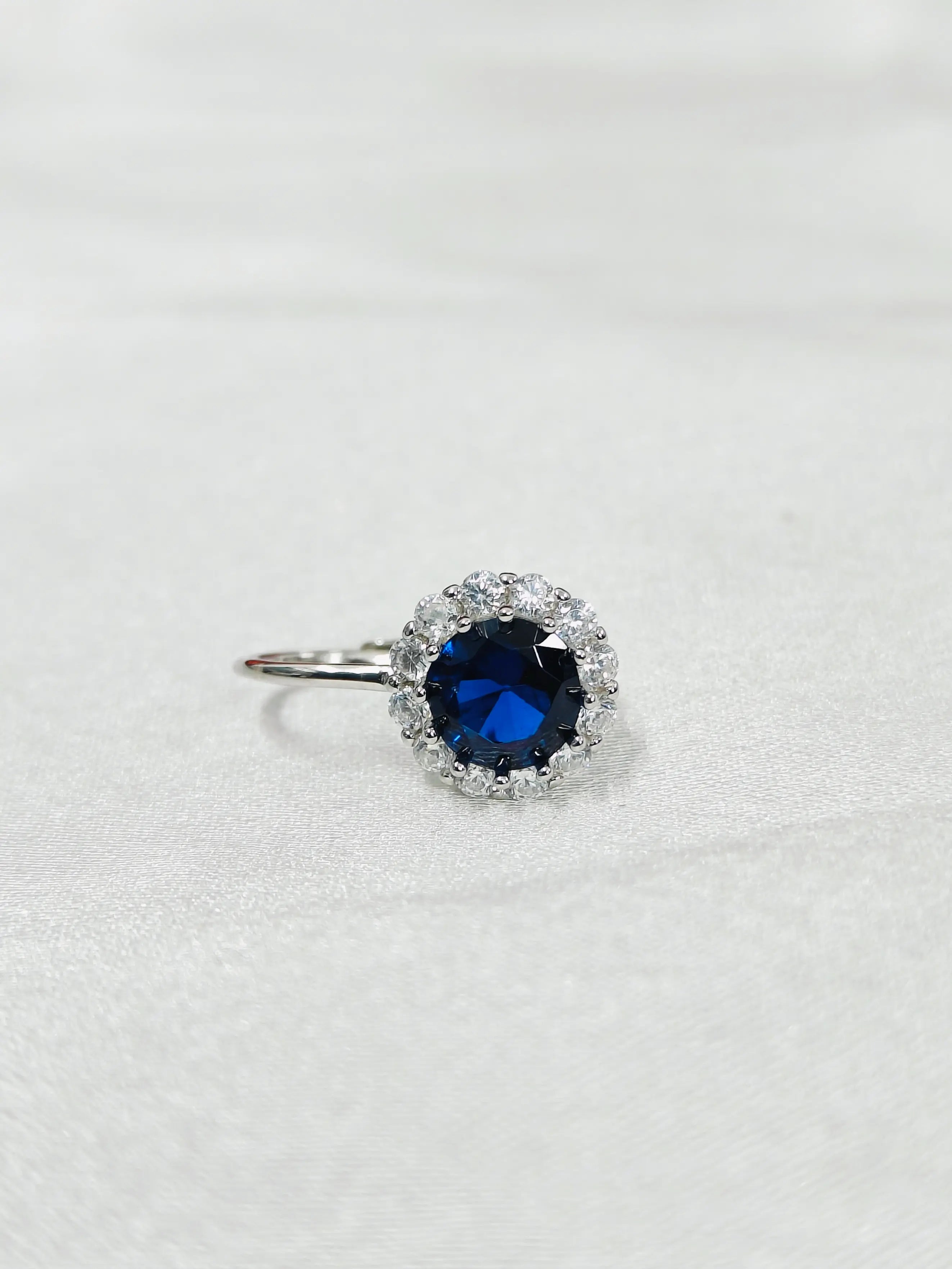 Ring with a blue gemstone and diamond-studded halo on a white background