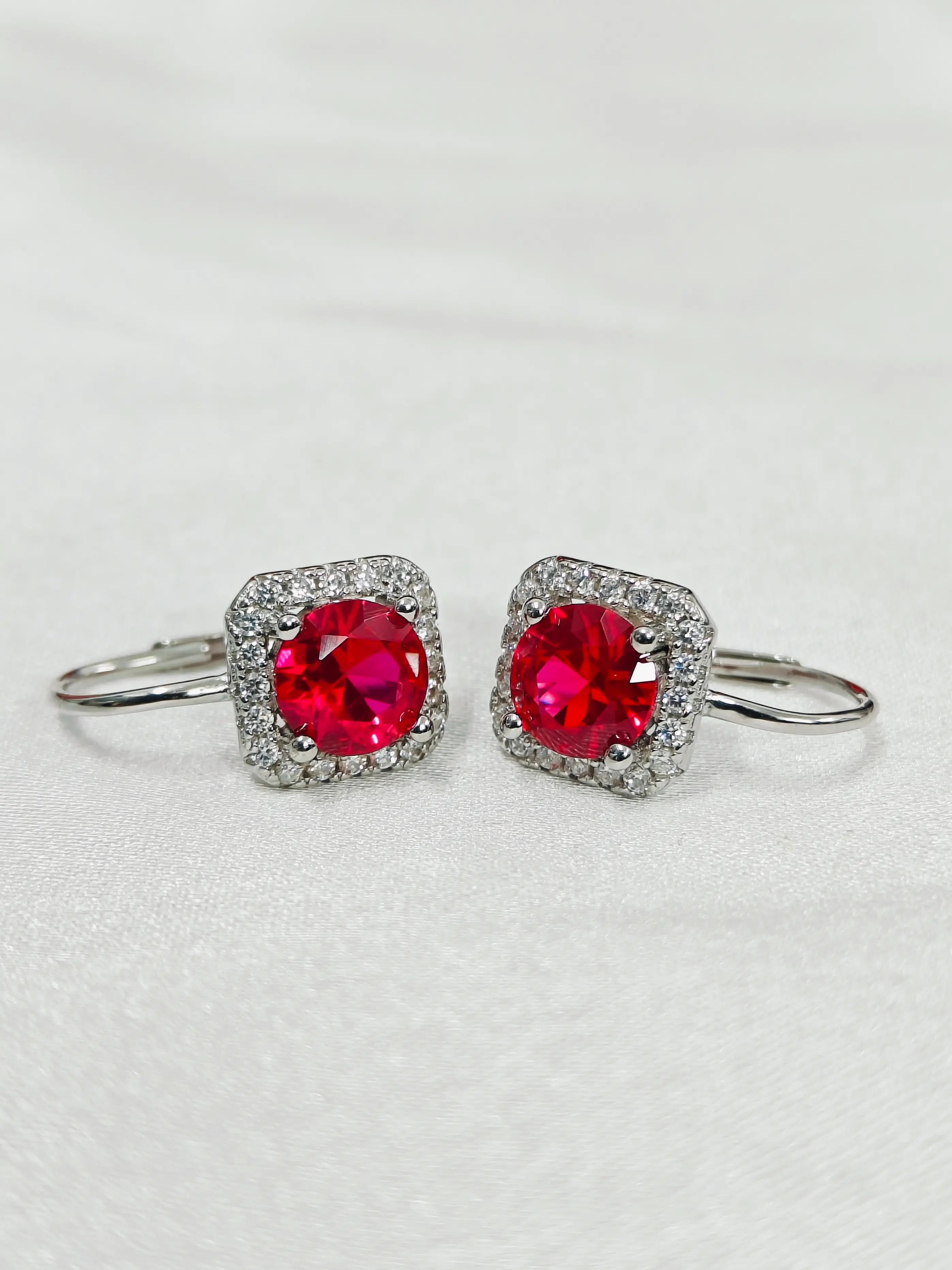 Pair of earrings with red gemstones and silver surrounds on a light gray background