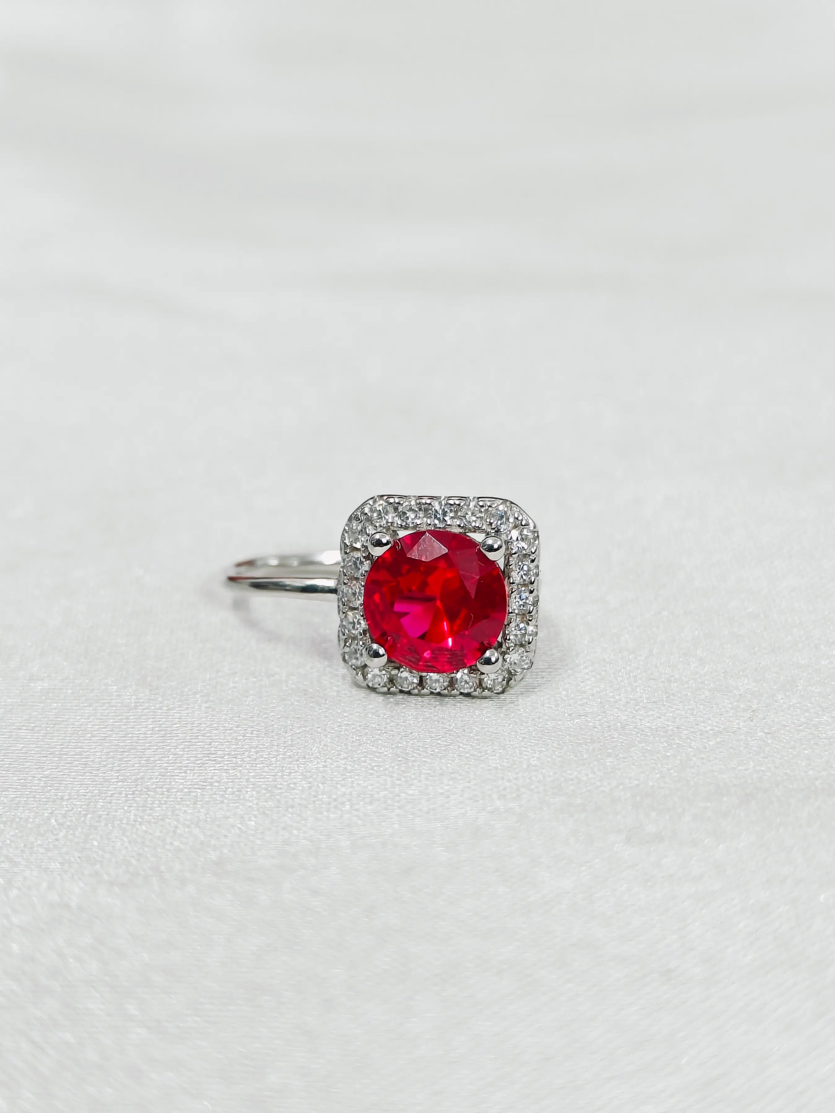 Ring with a red gemstone and diamond-studded band on a light gray background