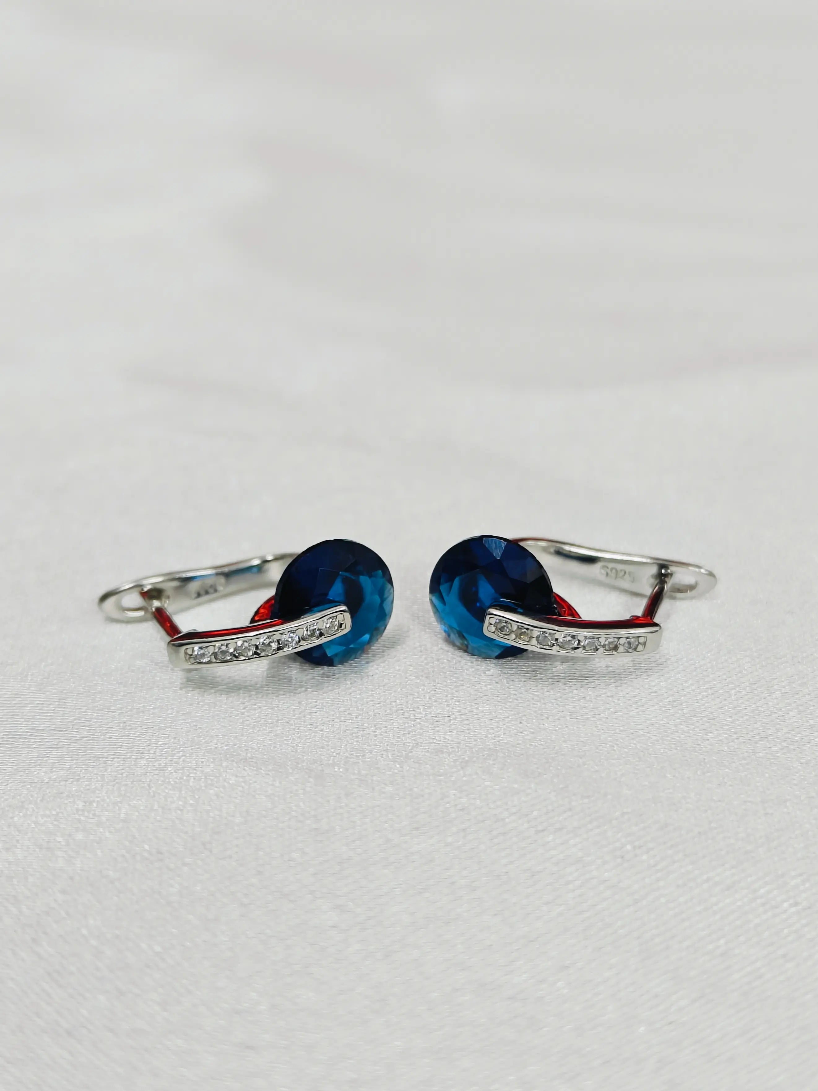 Pair of silver earrings with blue stones on a light gray background