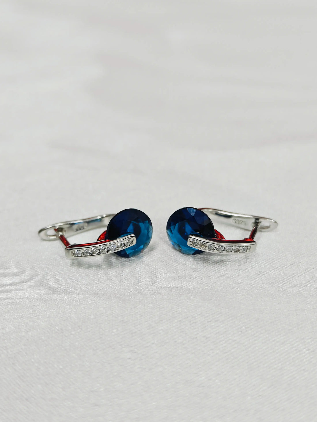 Pair of silver earrings with blue stones on a light gray background