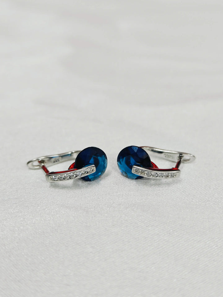 Pair of silver earrings with blue stones on a light gray background