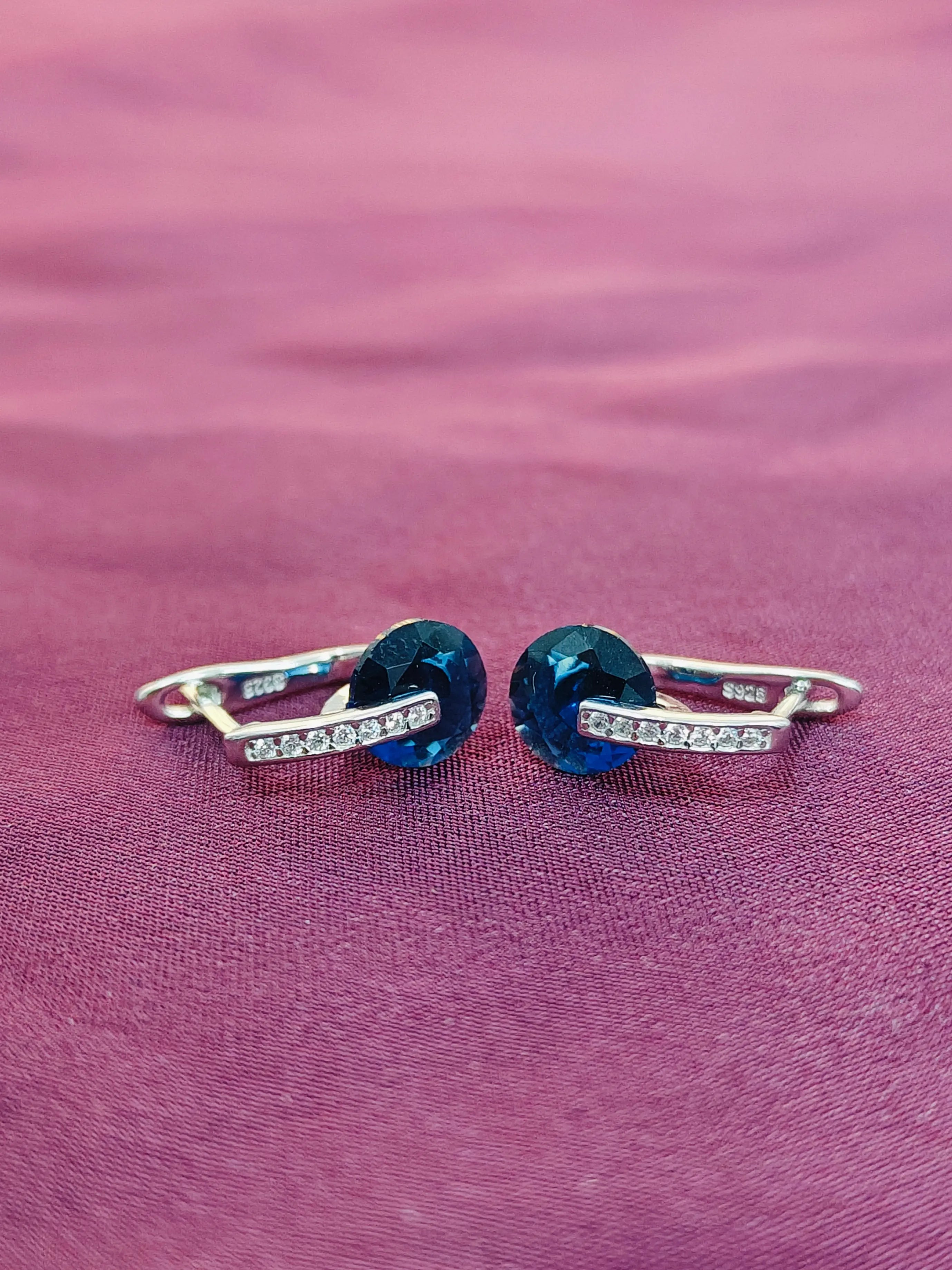 Pair of earrings with blue gemstones on a pink fabric background